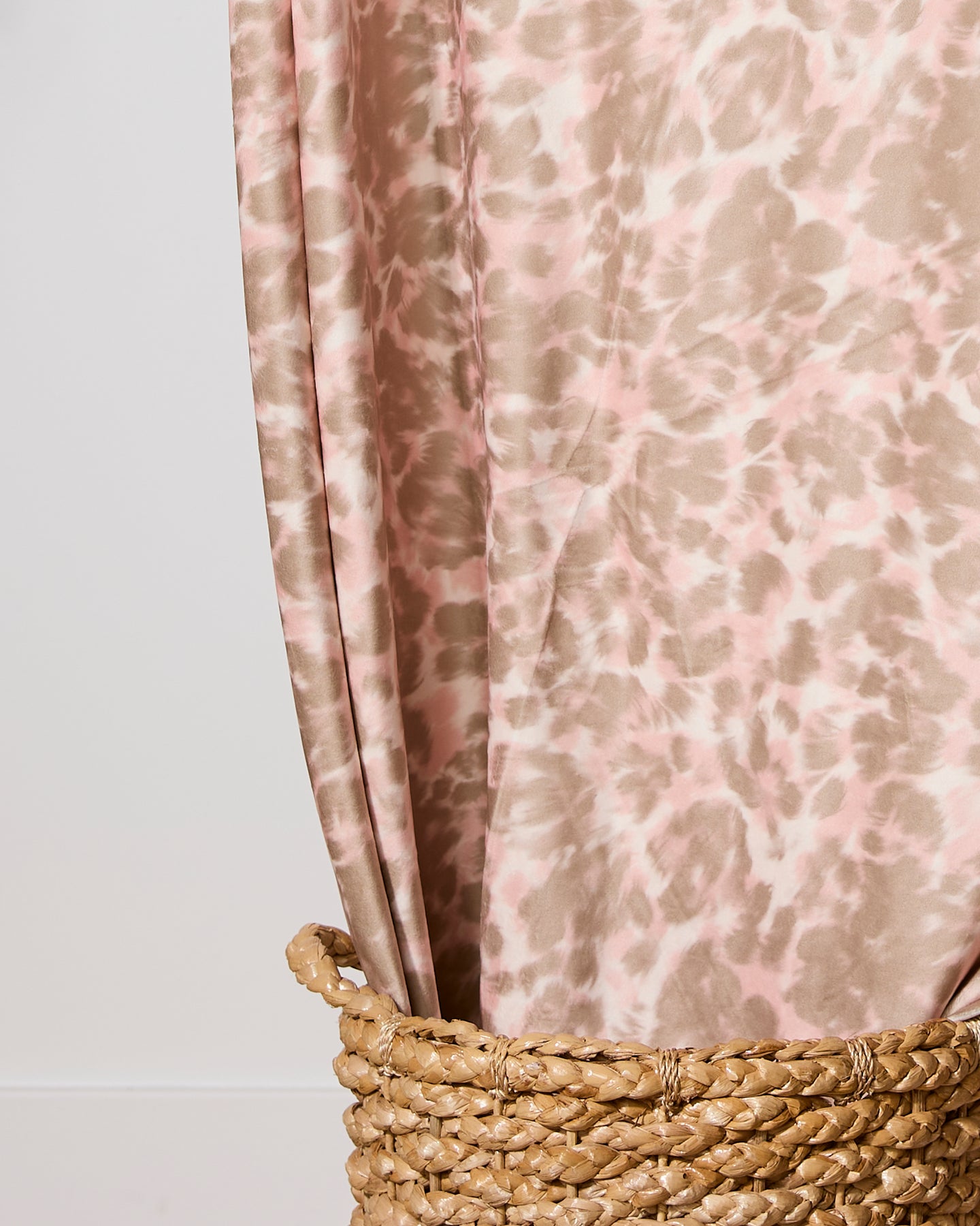 The Geometry Soft Umber blanket in a light pink and beige animal print is draped in a woven wicker basket against a plain white wall.