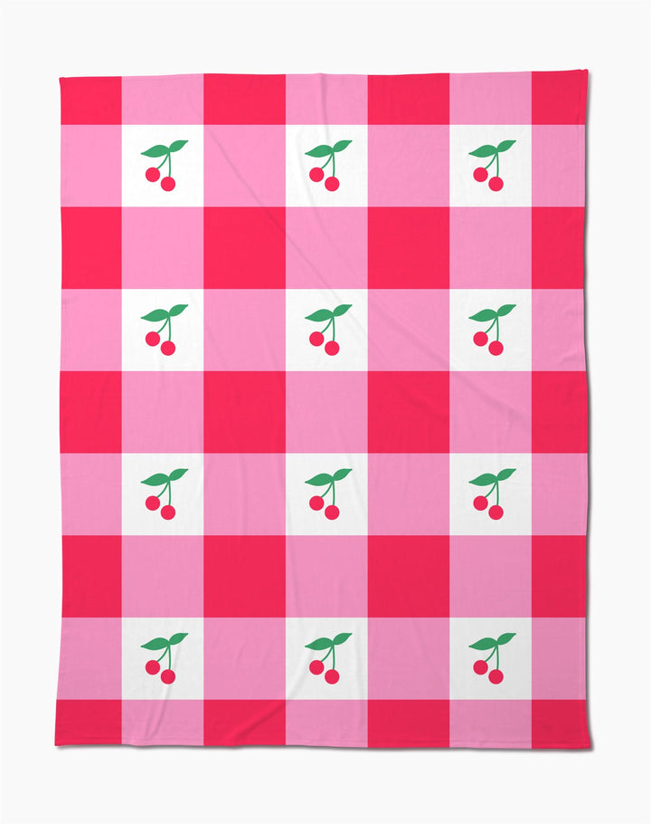 The Sweet Cherry Gingham throw blanket by Geometry features a soft fabric with a red and pink checkered pattern, accented by charming cherry illustrations with green leaves in the center of select squares.