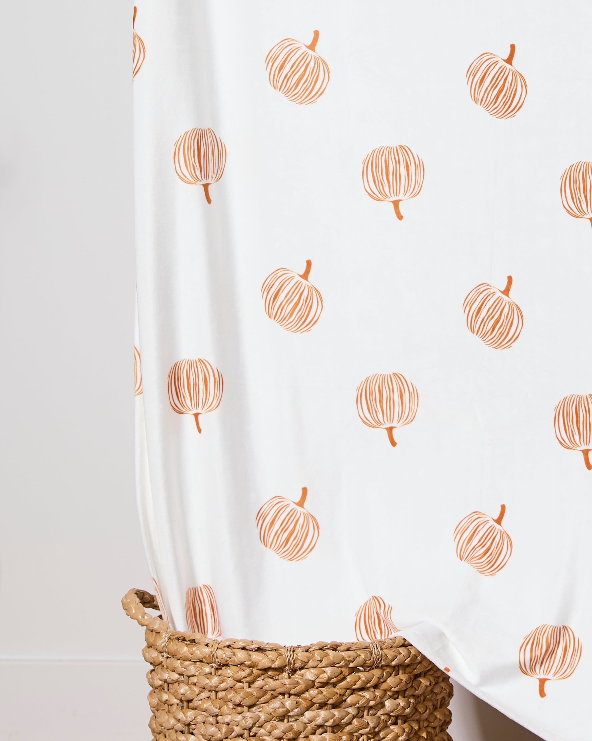 A Geometry Tales From the Patch Butter Blanket, featuring simple orange pumpkin illustrations, is draped over a woven basket.