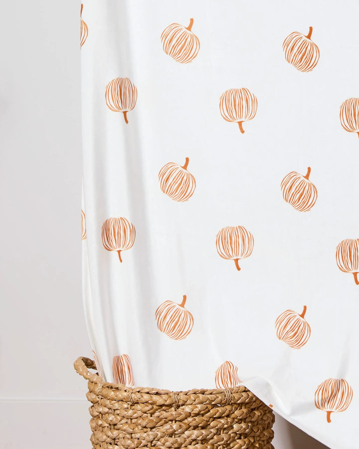 A Geometry Tales From the Patch Butter Blanket, featuring simple orange pumpkin illustrations, is draped over a woven basket.