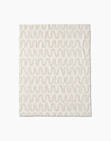 The Abstract Squiggles throw blanket by Geometry is crafted from recycled blankets for comfort and sustainability, featuring a soft cream color with evenly spaced wavy beige lines in a repeating pattern, displayed flat against a white background.