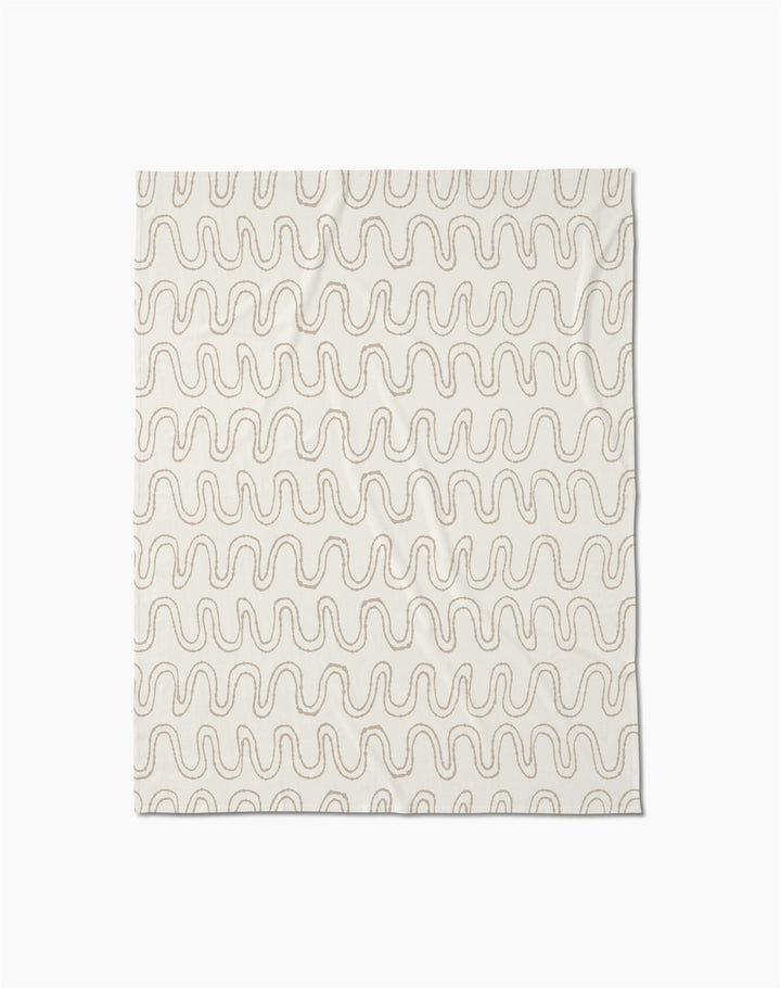 The Abstract Squiggles throw blanket by Geometry is crafted from recycled blankets for comfort and sustainability, featuring a soft cream color with evenly spaced wavy beige lines in a repeating pattern, displayed flat against a white background.