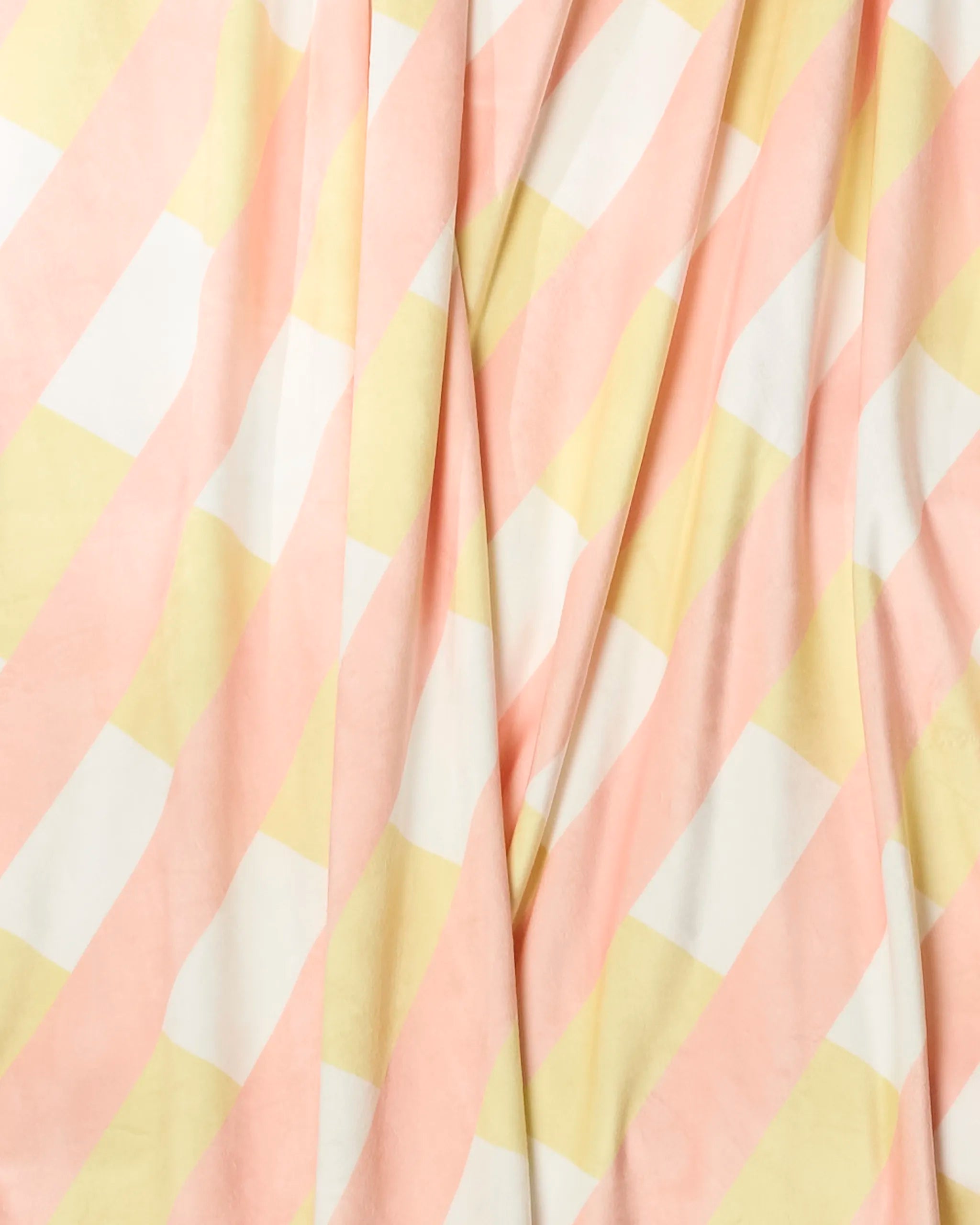 A close-up of Geometry’s Apricot Glow throw blanket shows its pastel pink, yellow, and white diagonal checkerboard pattern. The soft fabric displays gentle folds and a smooth texture.