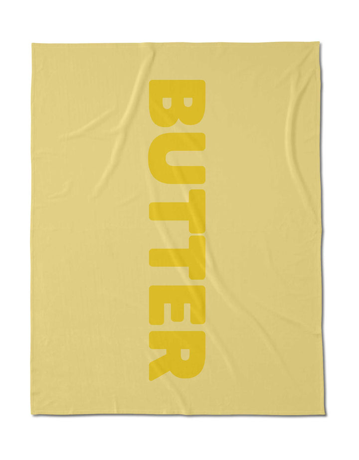 A yellow, silky-soft square cloth by Geometry, made from post-consumer recycled materials, features BUTTER in bold vertical letters down the right side.