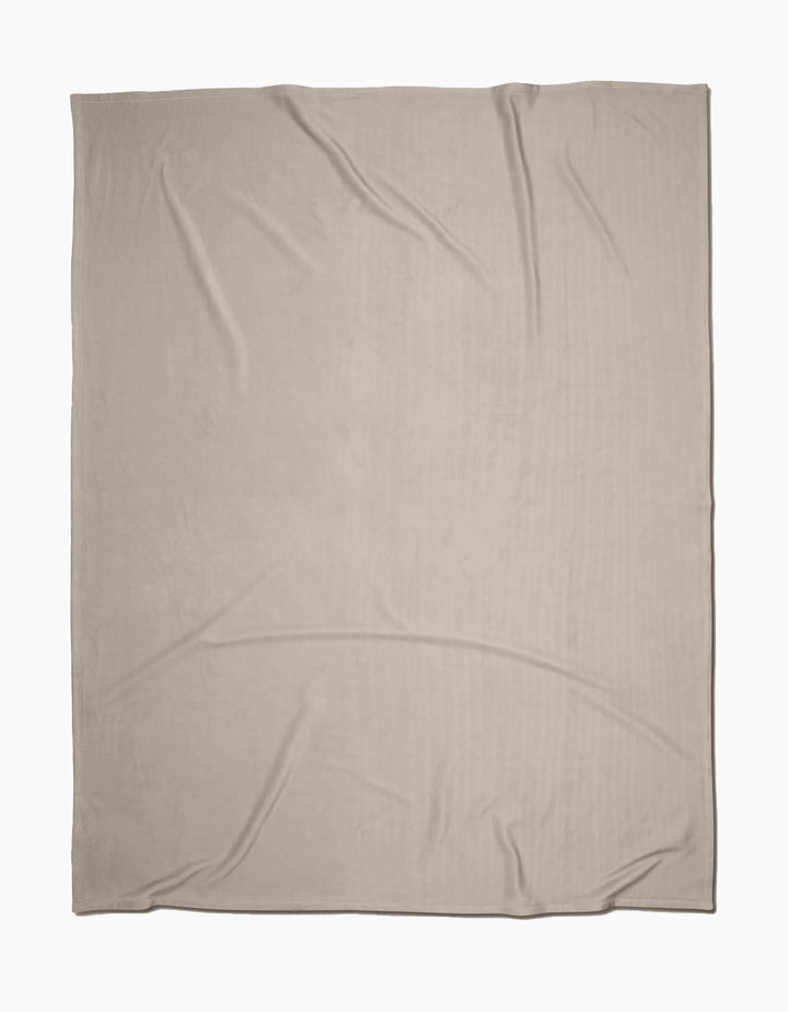 The GEOMETRY Desert Haze Butter Blanket, crafted from recycled materials in light beige with slight wrinkles, is laid flat on a white background.