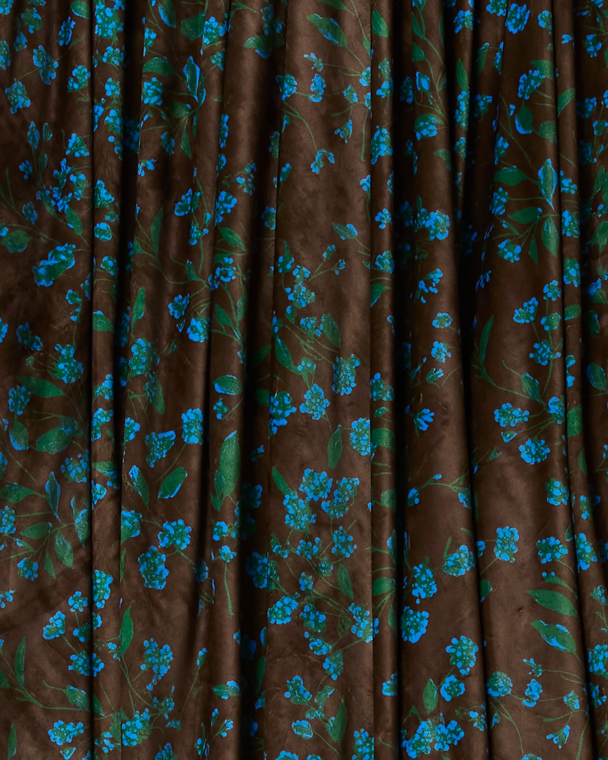 Floralie by Geometry is a dark brown fabric with a draped texture, adorned with small blue flowers and green leaves—crafted from recycled blankets for an eco-friendly, charming touch.