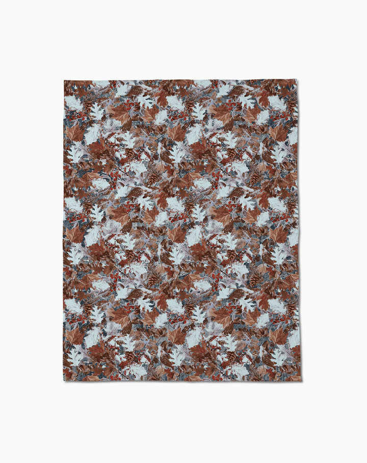 The Geometry Frosty Camo rug displays a dense, repeating pattern of brown, blue, and white leaves on a textured base for an autumn-inspired look. Shown on a plain white surface, its design evokes the feel of recycled blankets.