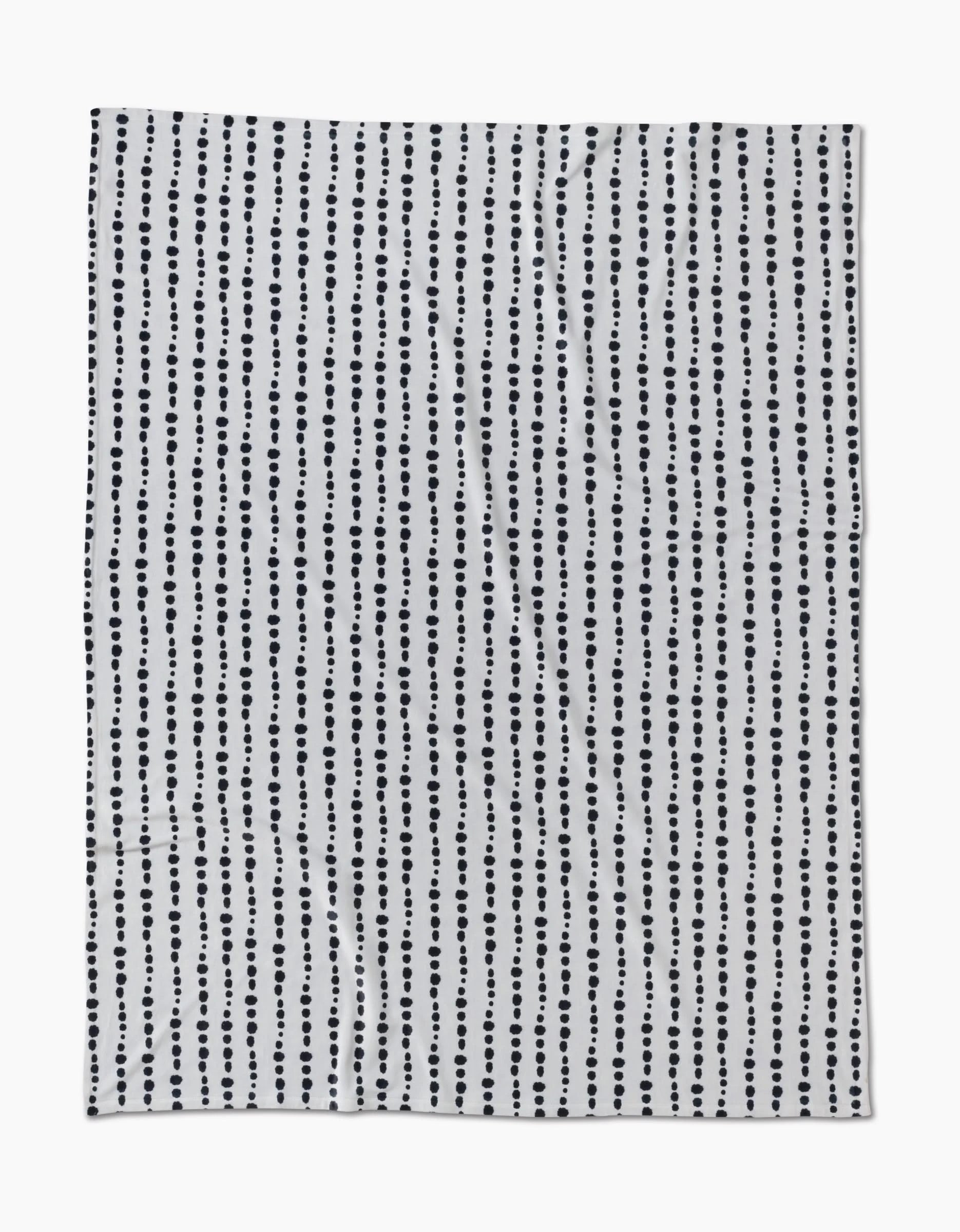 The Geometry Ink Dots Butter Blanket features vertical rows of evenly spaced black dots on white, offering a simple, modern polka dot design—crafted from recycled materials for an eco-friendly touch.