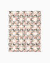The Russet Crossroads Butter Blanket by Charlie Rowan Designs features a geometric grid of black, red, and cream squares on white, crafted from recycled materials for an eco-friendly touch.