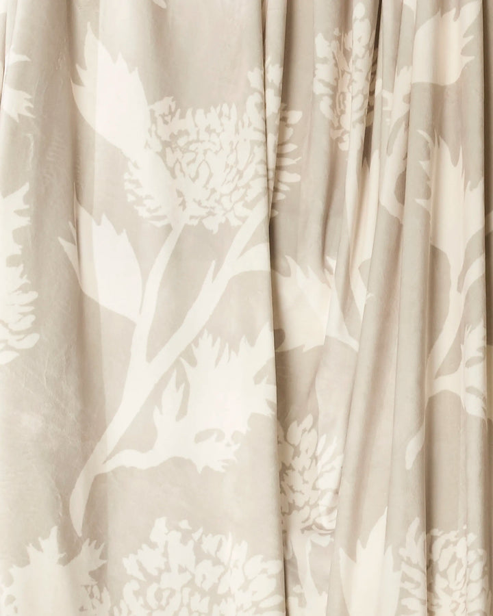 The Geometry Soft Blooming Thistle throw blanket features beige and cream fabric with a subtle thistle floral pattern, adding cozy style and gentle elegance to any space.