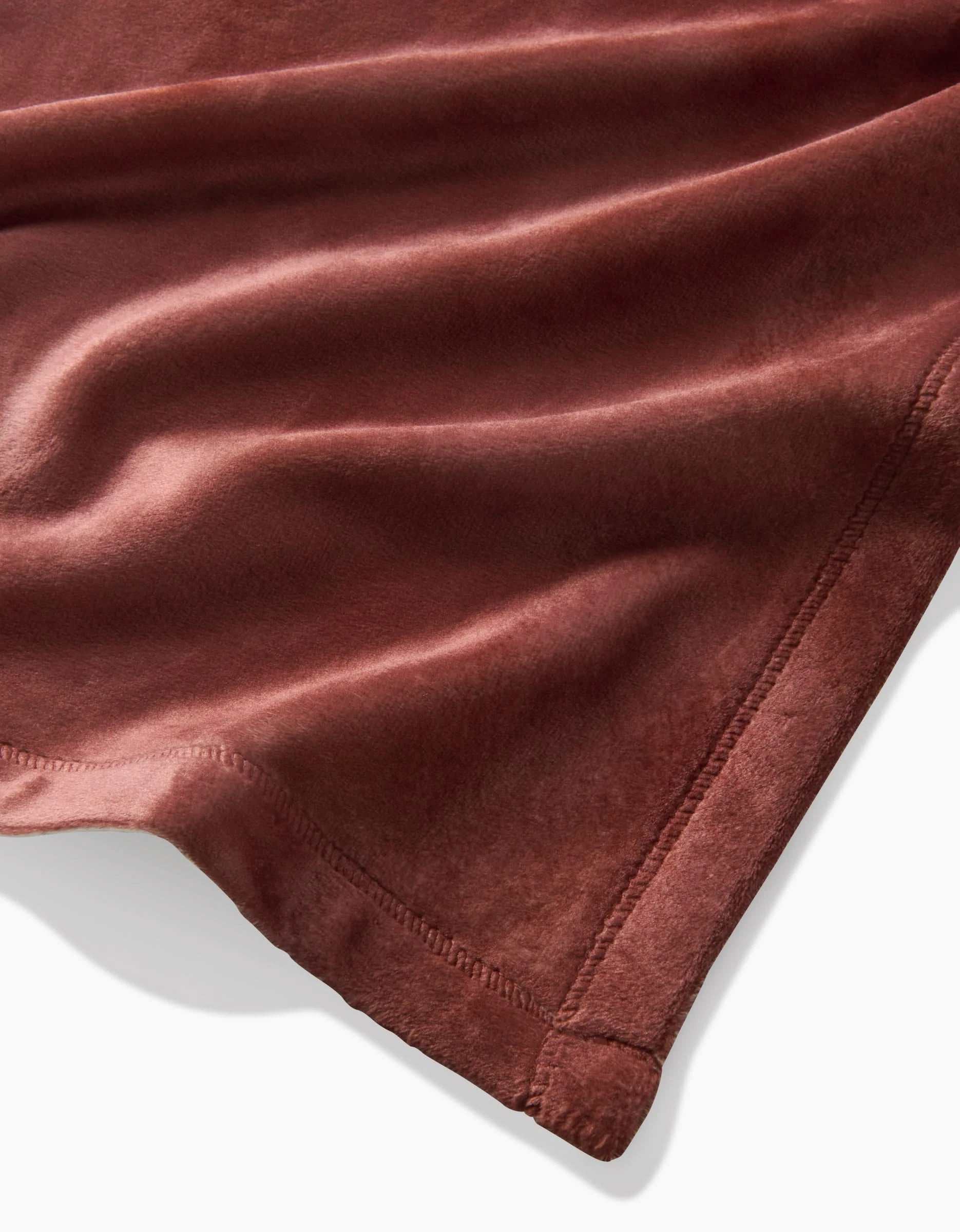 A close-up of the Sundae blanket by Geometry, featuring soft, reddish-brown eco-friendly velvet with smooth wavy folds and neatly stitched edges.