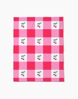 The Geometry Sweet Cherry Gingham throw blanket features a pink and red checkered pattern with white squares, each adorned with two red cherries and green leaves—adding cozy, cheerful comfort to any space.