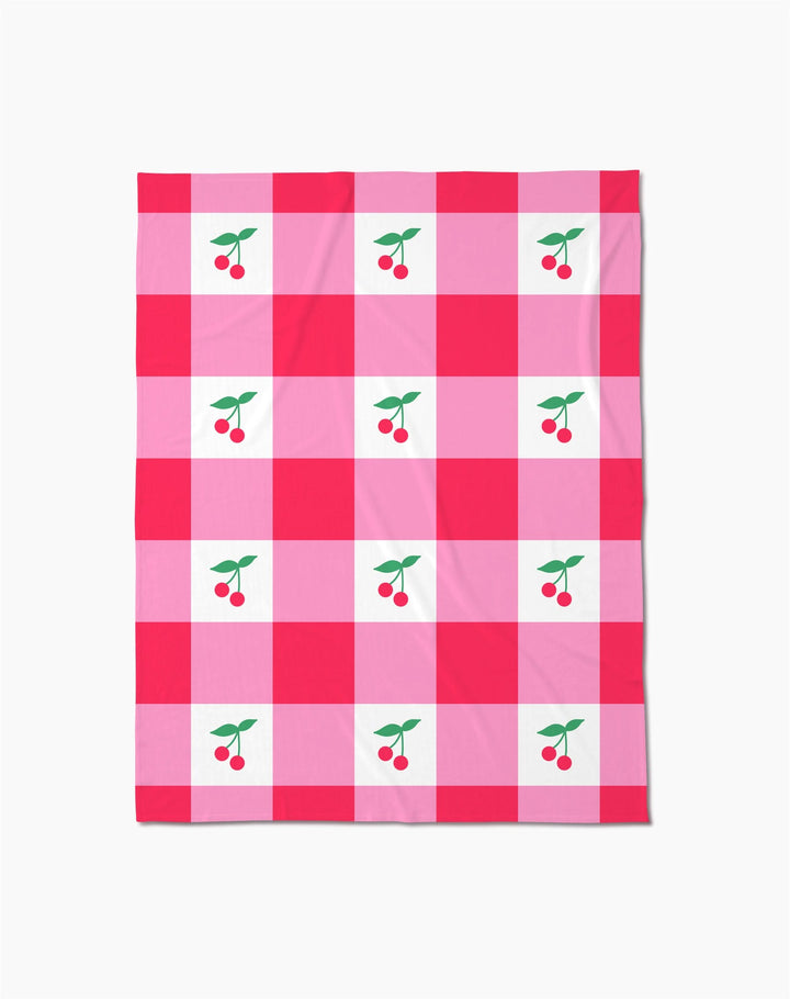 The Geometry Sweet Cherry Gingham throw blanket features a pink and red checkered pattern with white squares, each adorned with two red cherries and green leaves—adding cozy, cheerful comfort to any space.