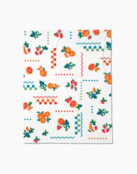 The Aubrey Fairchild Sweet Pickings Butter Blanket offers silky softness with a vibrant design of oranges, strawberries, leaves, and colorful geometric shapes in red, blue, and green.