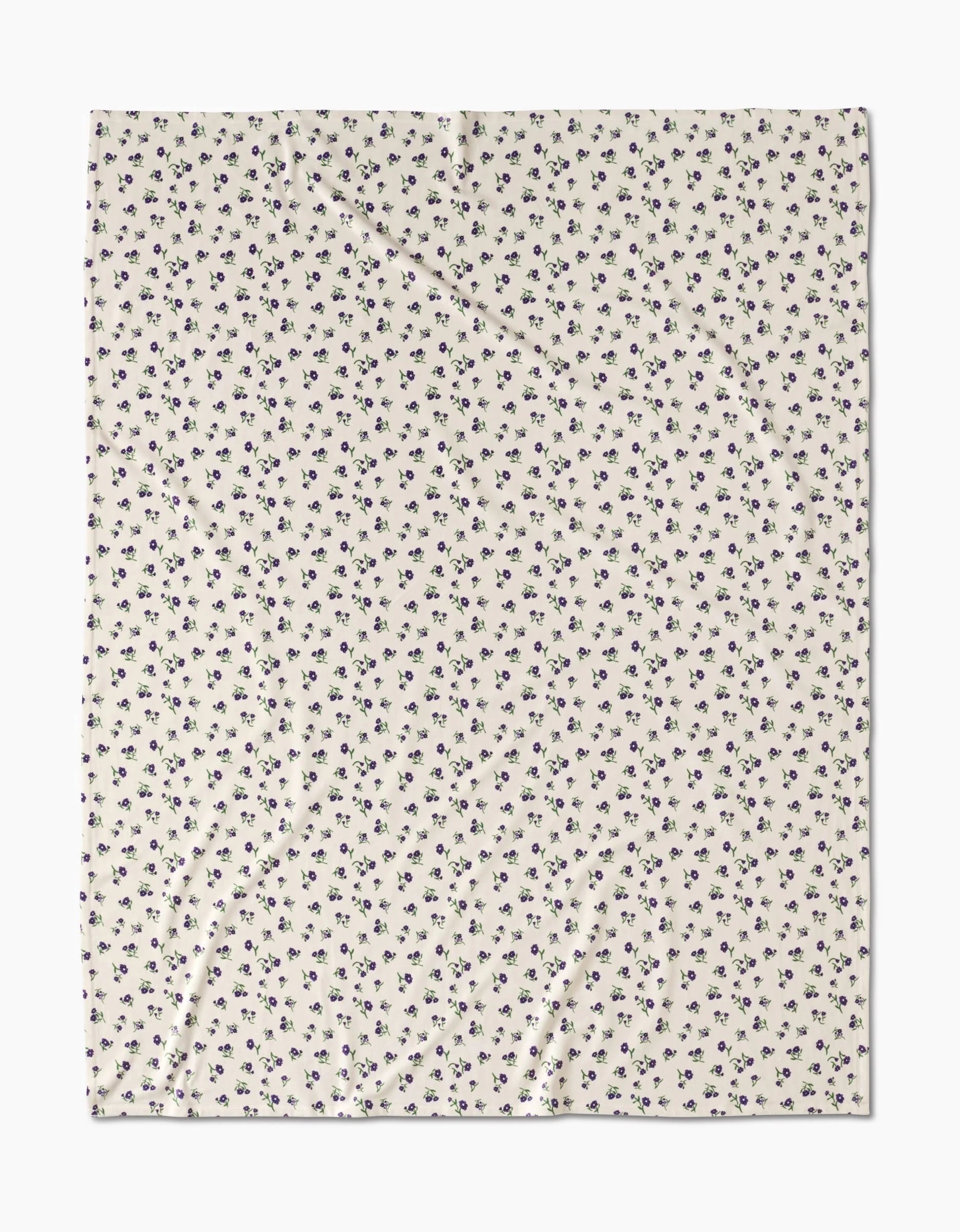 The Violet Sound by Geometry is a rectangular cream-colored blanket featuring a repeating small dark blue floral pattern, laid flat with subtle wrinkles—crafted from recycled materials for sustainability.