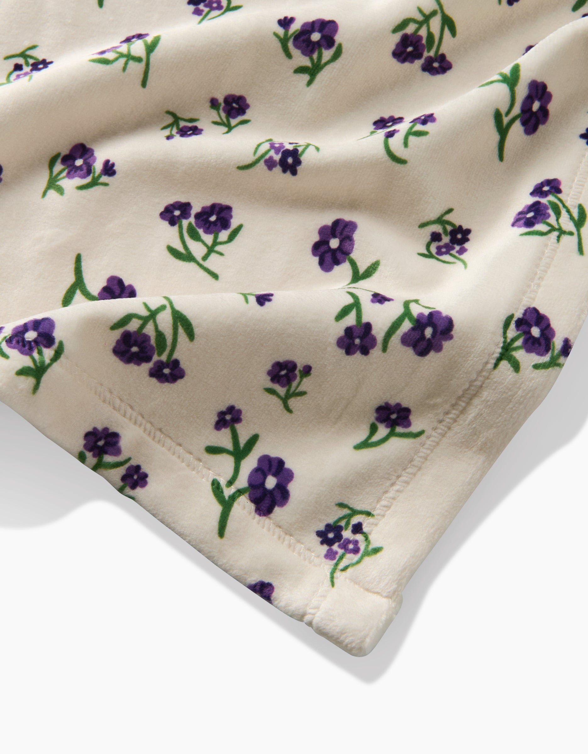 The Violet Sound by Geometry is a cream-colored Butter Blanket made from recycled materials, featuring purple flowers and green stems with neat stitching. Its soft, plush fabric is perfect for cozy, sustainable blankets or comfy clothing.