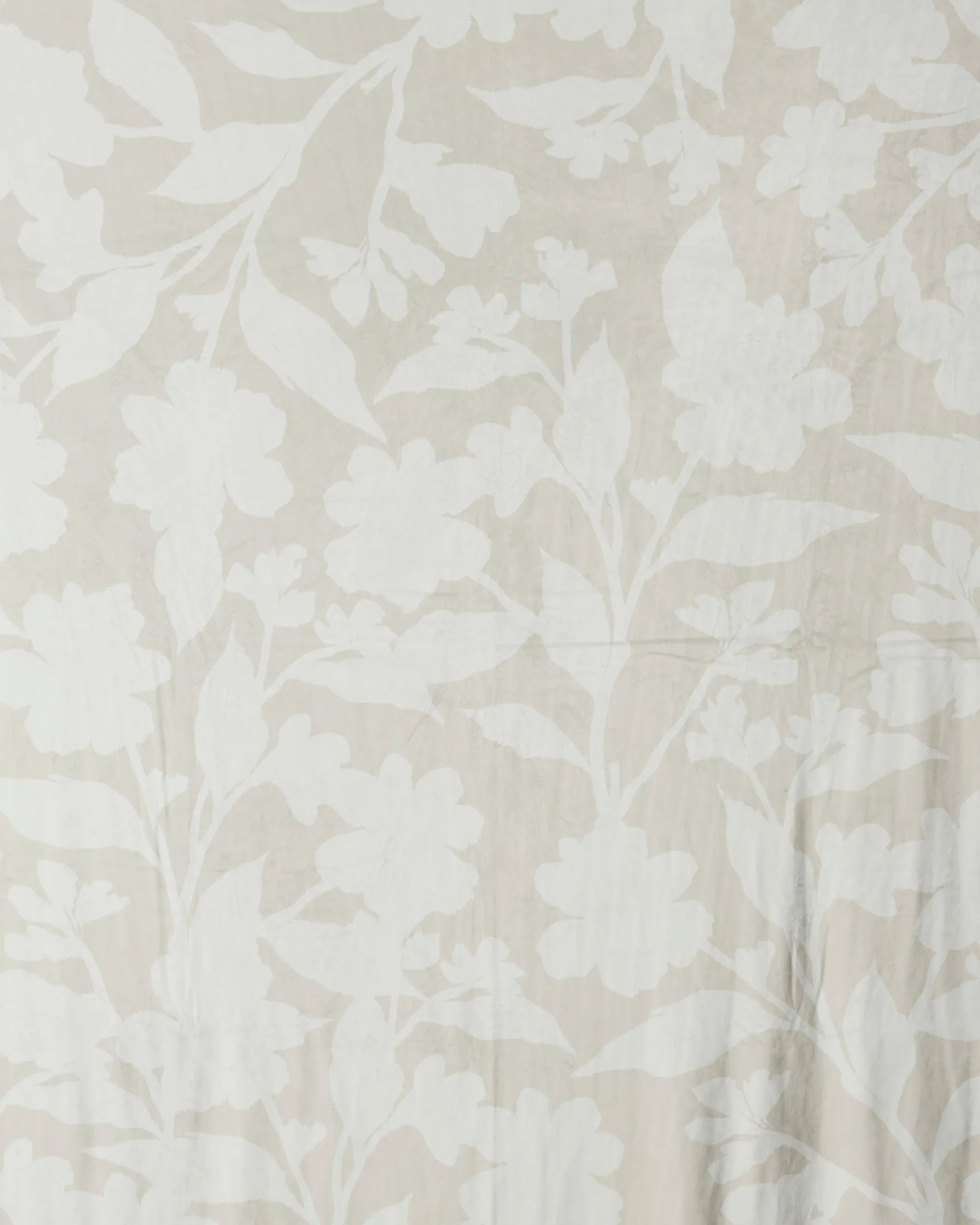 Geometry's Whispering Petals features cream-colored Butter Blanket fabric with a large, subtle white floral pattern of overlapping leaves and blossoms, creating a silky soft decorative blanket.