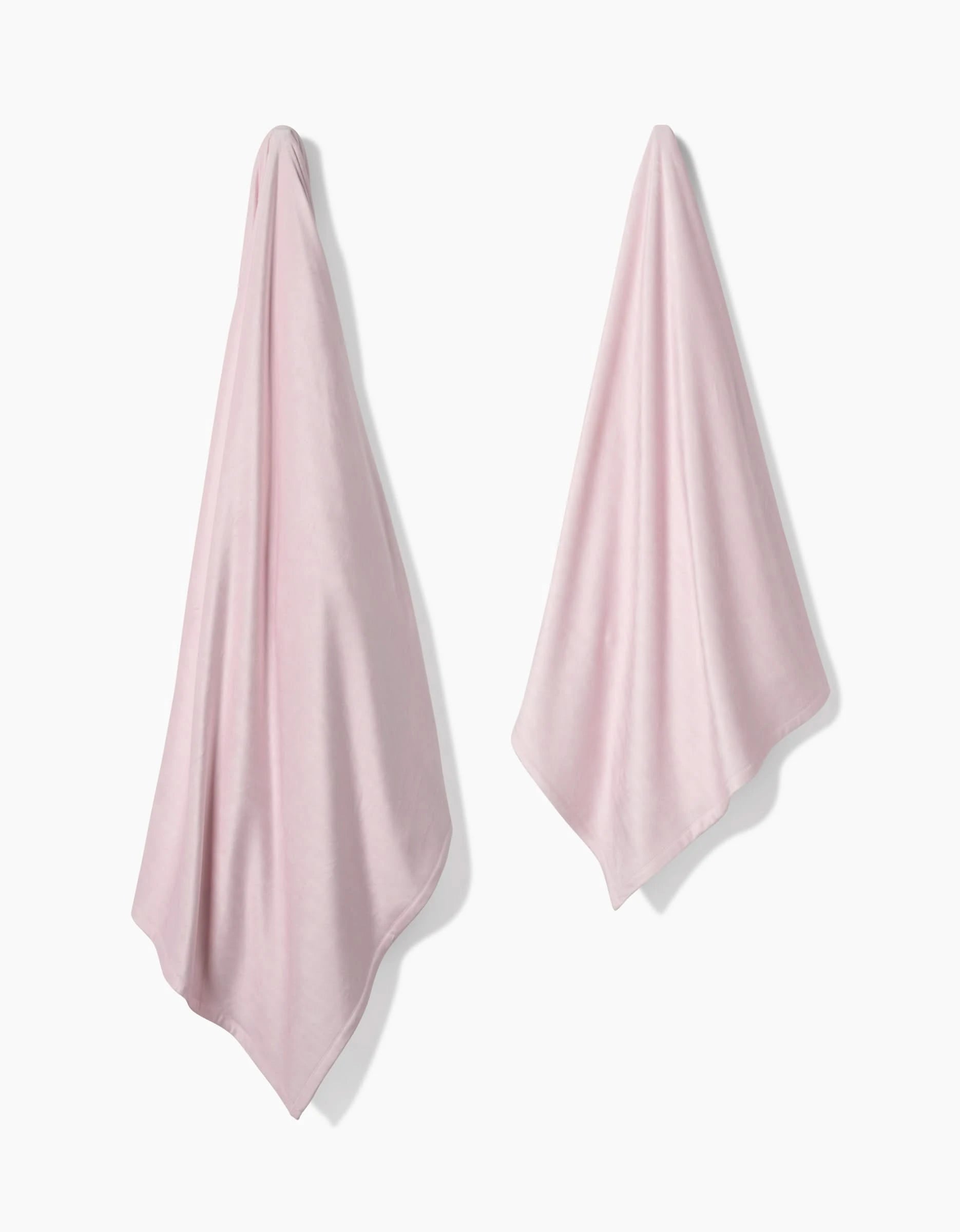 Two Berry Shortcake towels by GEOMETRY, crafted from post-consumer recycled materials, hang separately on a plain white background. Their light pink color and elegant folds convey silky softness and refined design.