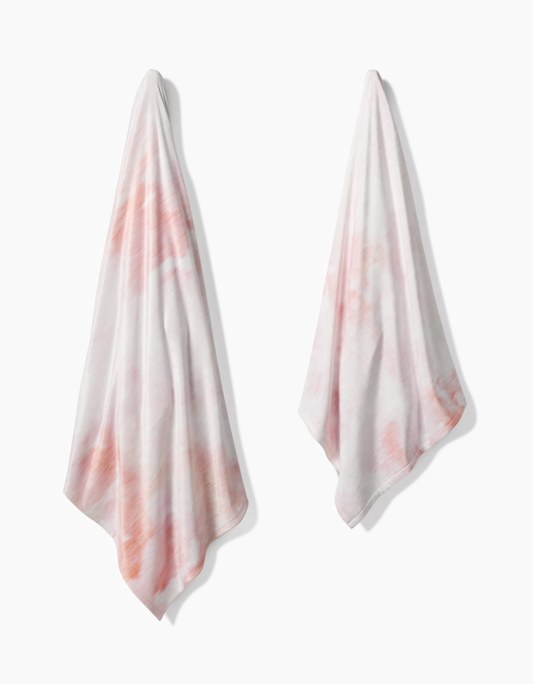 Two In the Clouds towels by Geometry, featuring a pink and white tie-dye pattern, hang side by side on a white background. Made from recycled materials, they offer silky softness inspired by the Butter Blanket collection.
