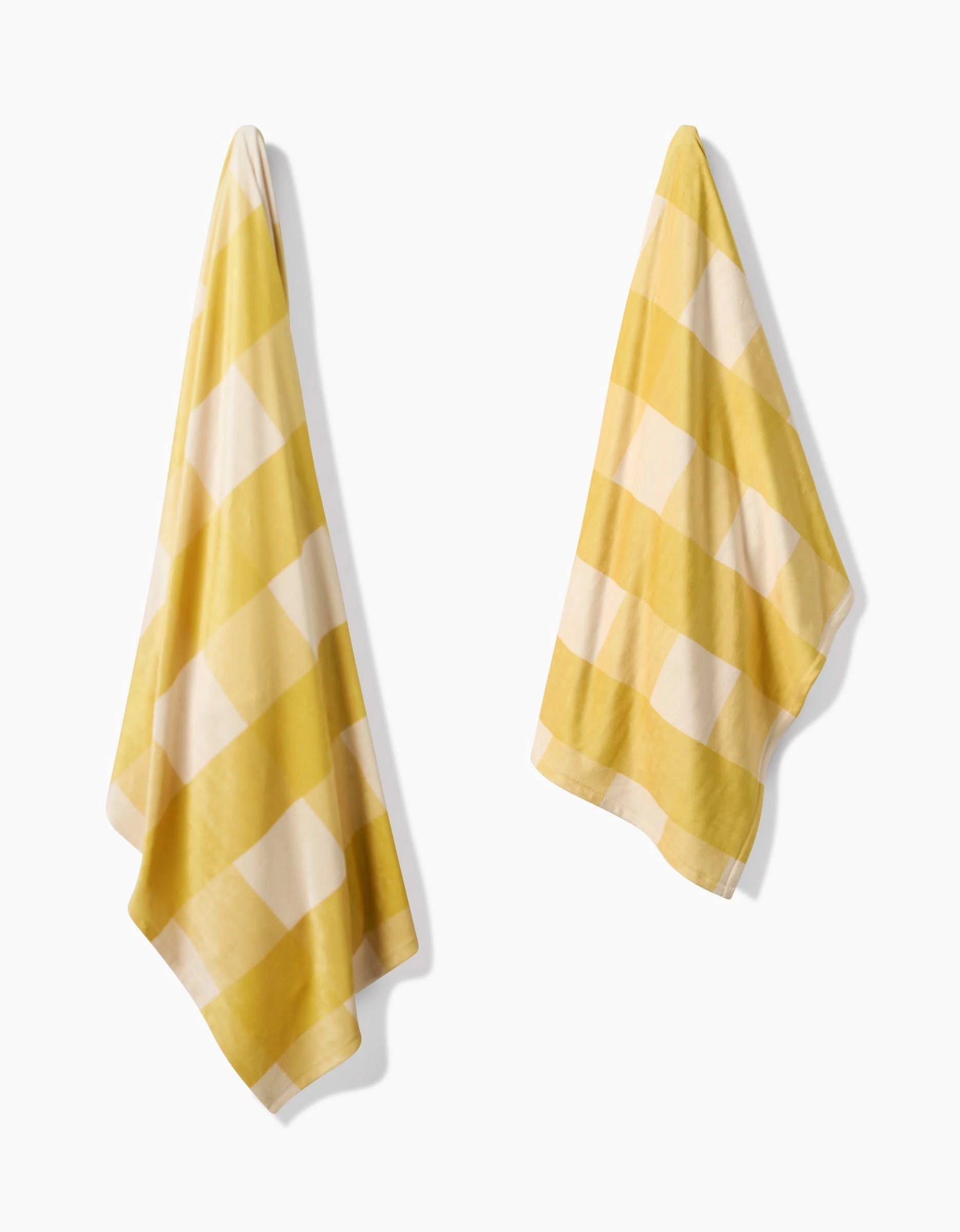 Two Lemonade Gingham towels by Geometry, featuring yellow and white checkered patterns, hang side by side against a white background, evoking the cozy feel of eco-friendly blankets.