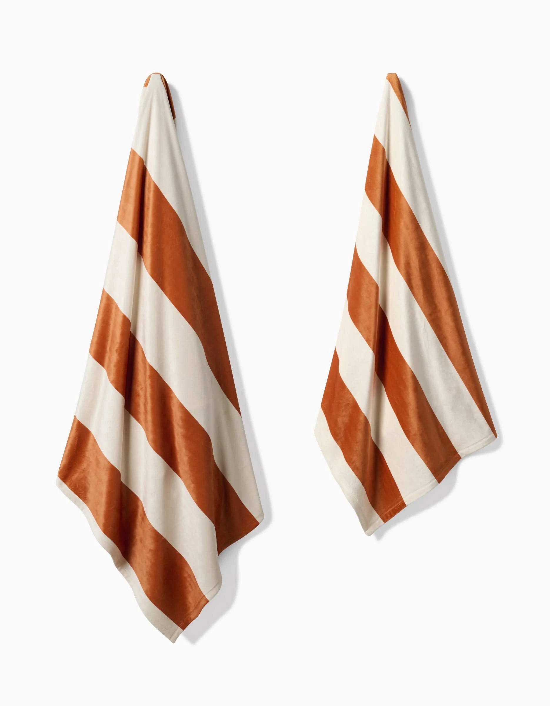 Two Geometry Radiance towels, made from recycled materials and featuring wide diagonal white and rust orange stripes, hang side by side against a plain white background.