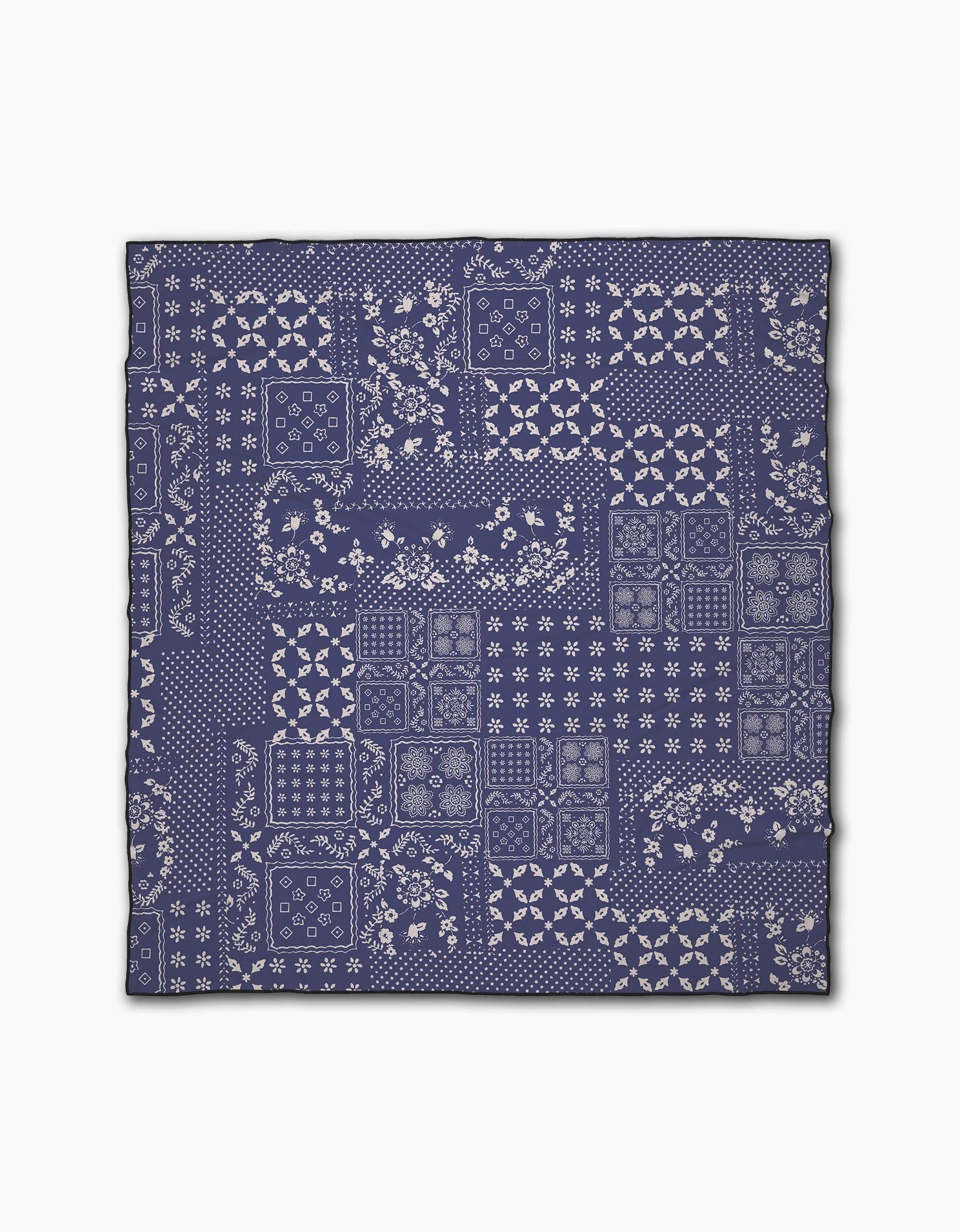 The Geometry Blossoming Bandanna Blue beach blanket features a navy blue and white patchwork pattern of floral and geometric designs in a quilt-like layout, made from quick-drying recycled materials, displayed on a white background.