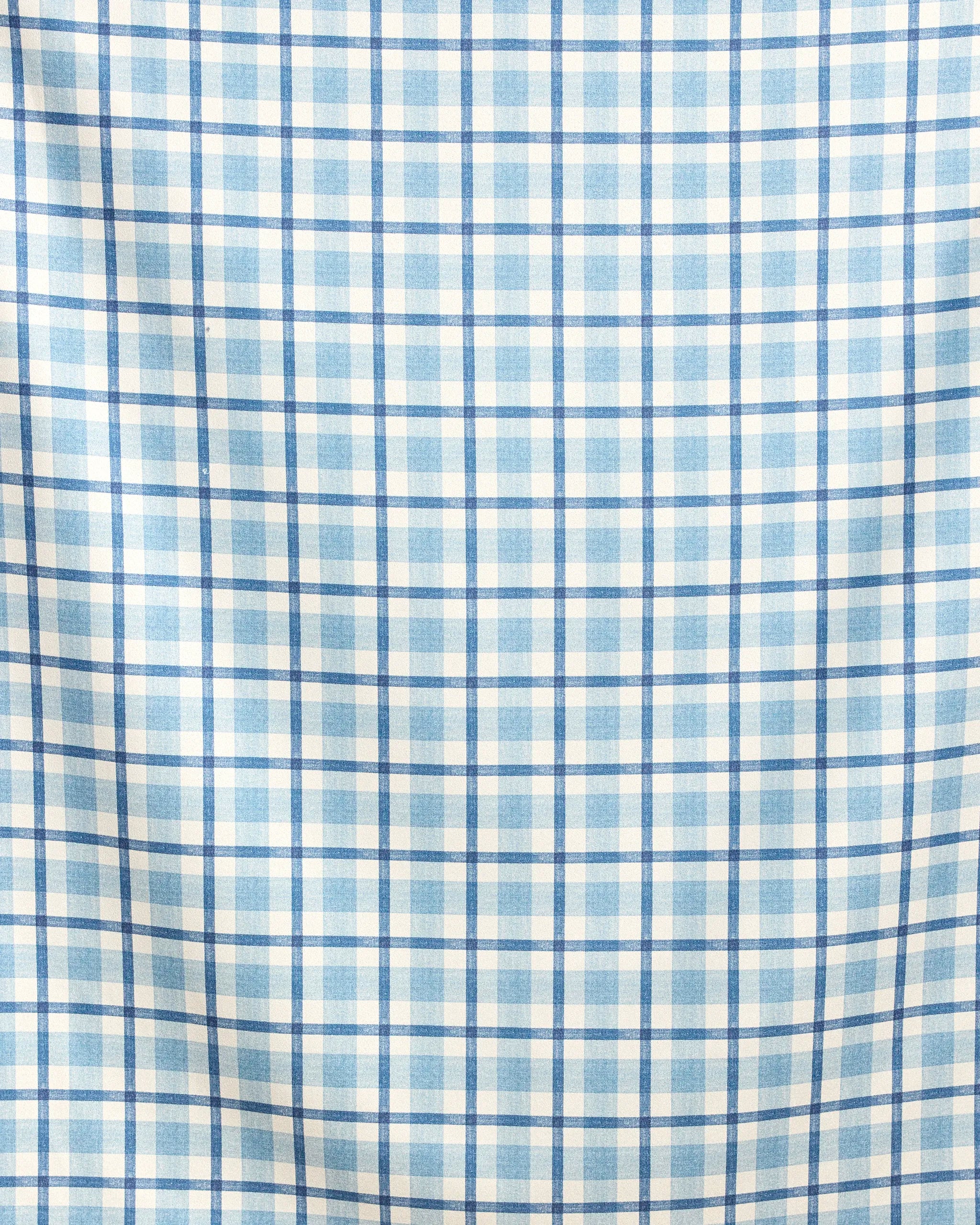 A close-up of Geometry's Bluefield beach blanket shows its light blue and white plaid fabric with evenly spaced lines. Slight wrinkles highlight its quick-drying comfort and convenient design.