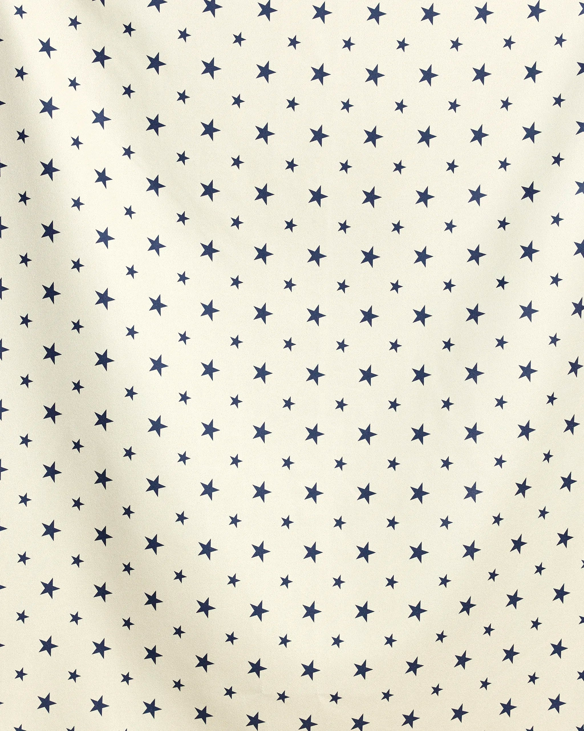 Boardwalk Star by Geometry features a beige background with a repeating pattern of small, evenly spaced dark blue stars and subtle folds, hinting at its quick-drying fabric—ideal for use as a beach blanket.