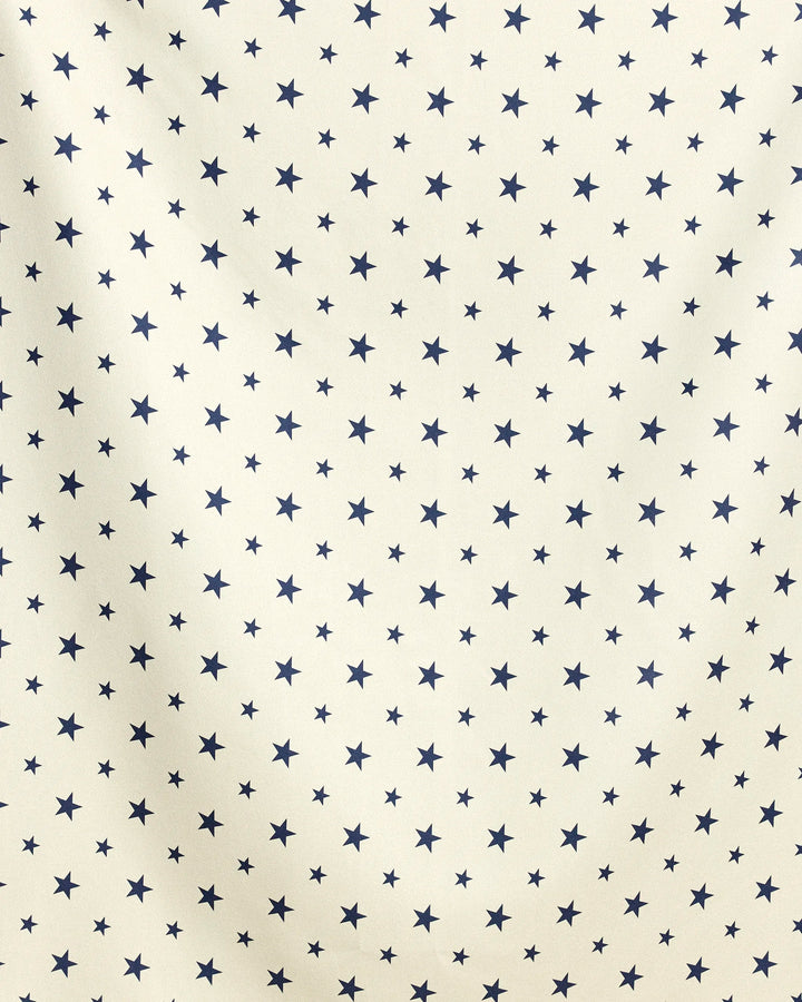 Boardwalk Star by Geometry features a beige background with a repeating pattern of small, evenly spaced dark blue stars and subtle folds, hinting at its quick-drying fabric—ideal for use as a beach blanket.