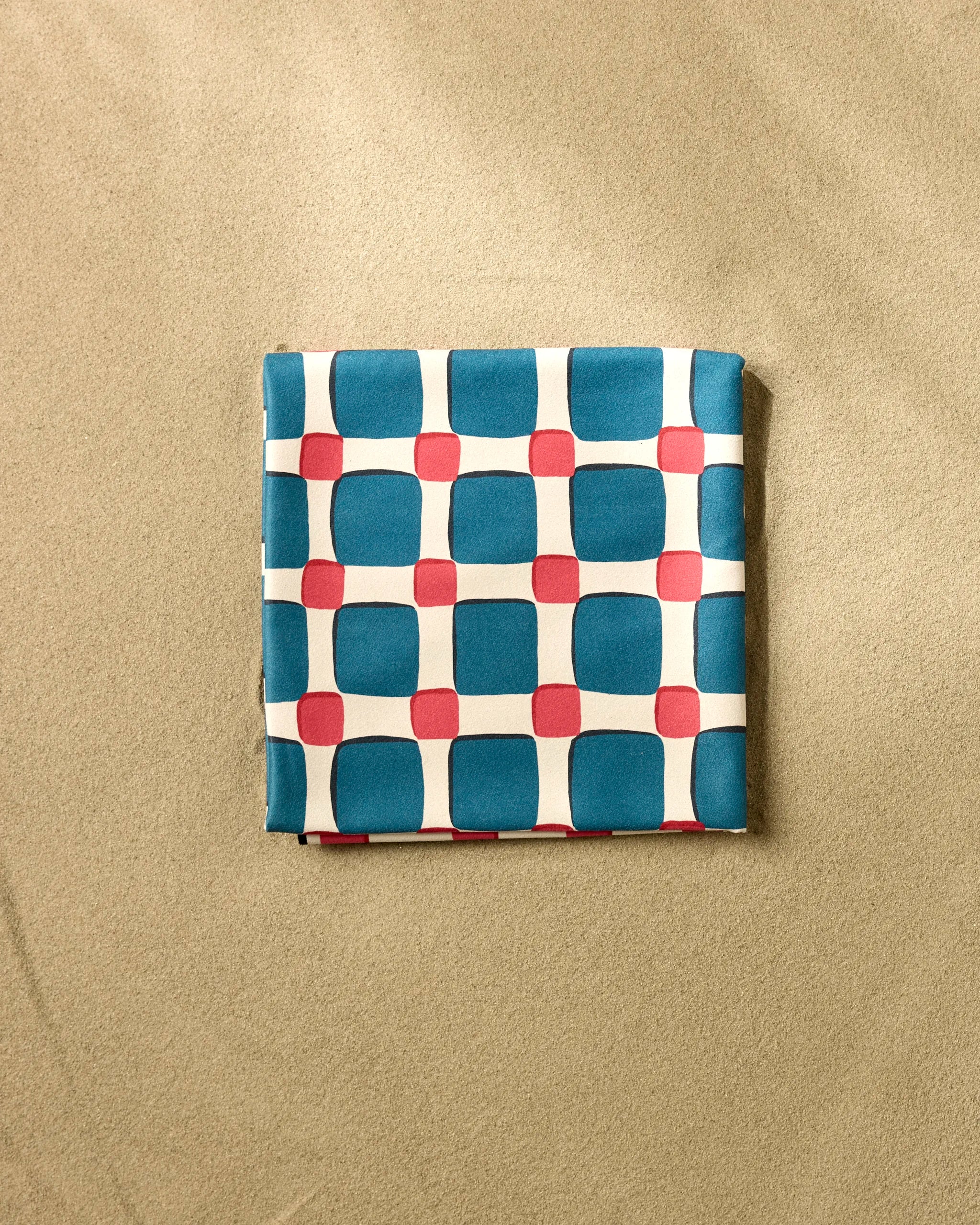 The Box Check Picnic by Hufton Studio is a micro-loop beach blanket featuring blue squares and red circles on white, neatly folded on a light brown textured surface.