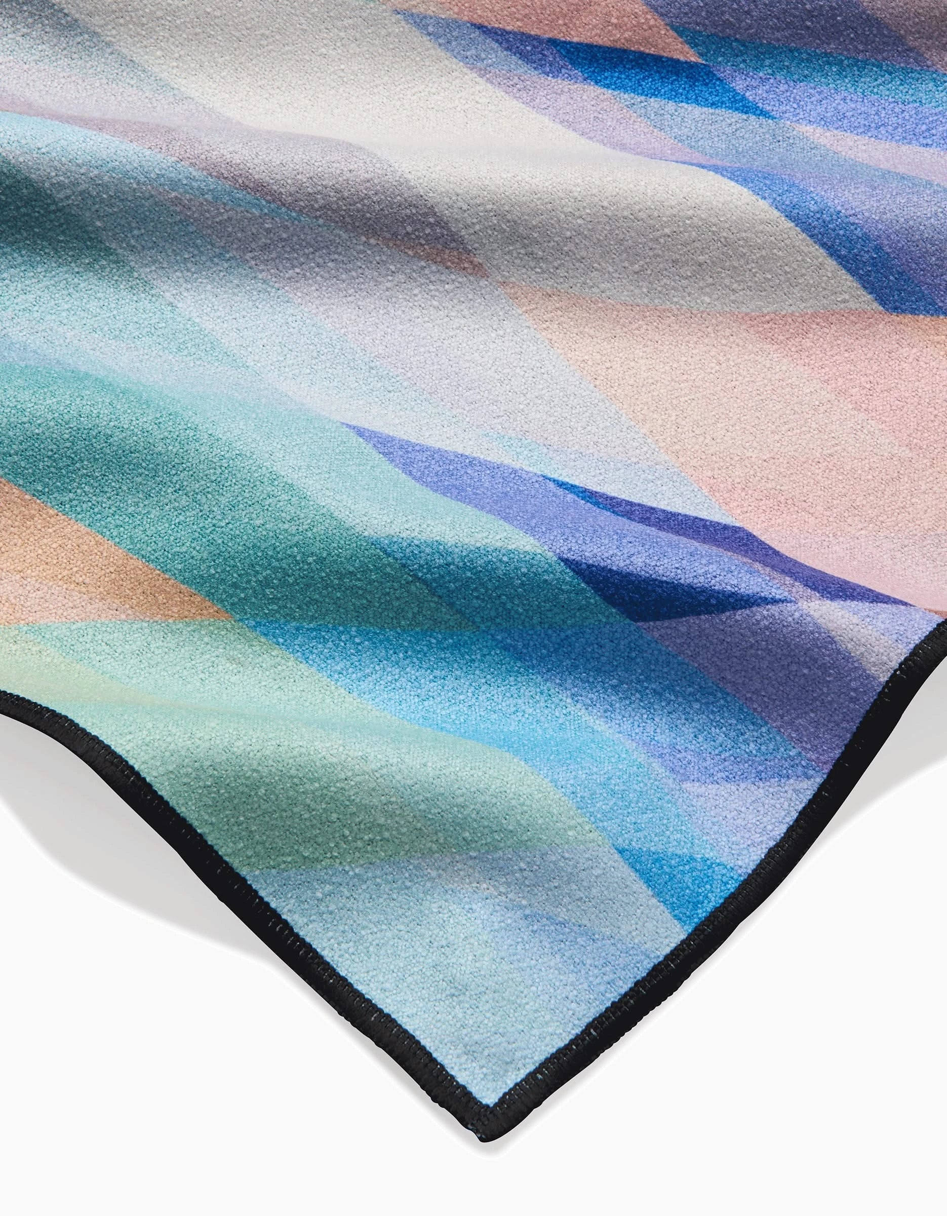 A close-up of Eventide by Rachel Parker: a soft, textured fabric with pastel geometric patterns and black trim, crafted from quick-drying recycled materials—the perfect compact beach blanket.