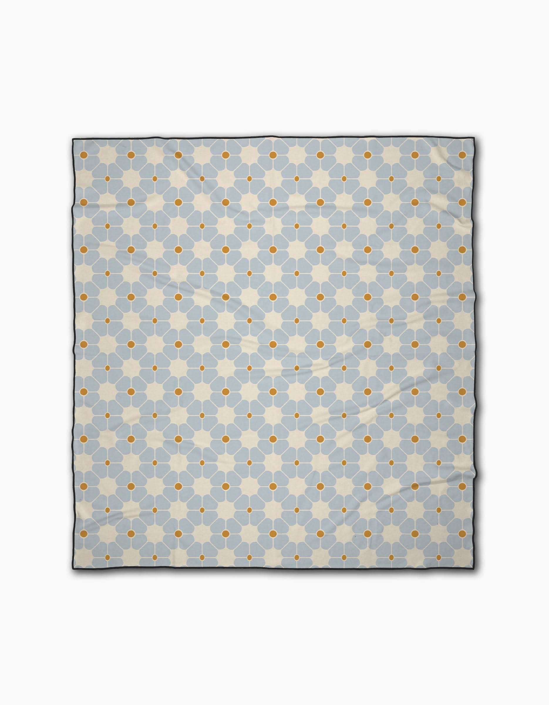 The Geometry Flora Tile Light Blue is a quick-drying beach blanket with a repeating geometric pattern of light blue hexagons and small orange circles on a white background.