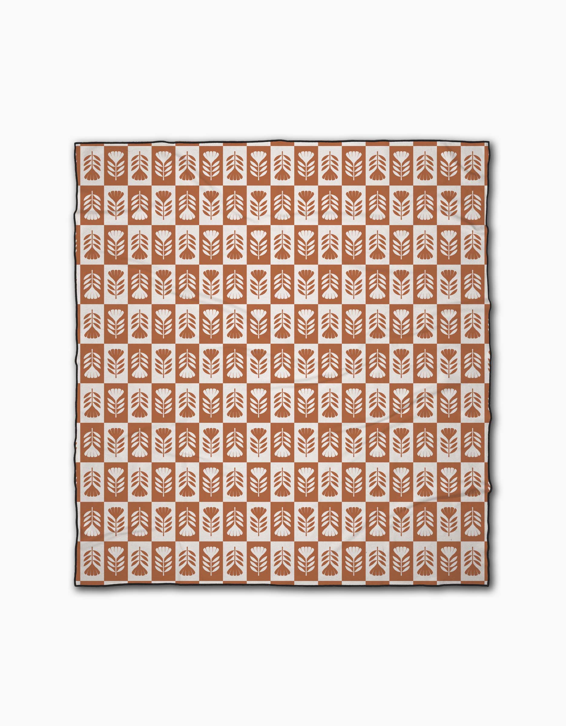 The Flower Patch Beach Blanket by Charlie Rowan Designs is a square micro-loop blanket displaying orange squares with white stylized leaf patterns, arranged in a grid on a white background.
