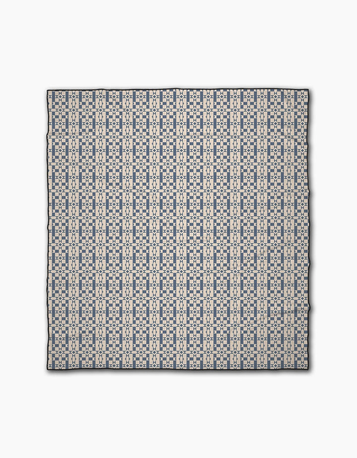 The Intermission Blue scarf by Geometry features a repeating geometric pattern in navy and light beige on white, made from recycled materials. Symmetrical lines and shapes add style as it lays flat on a white surface.