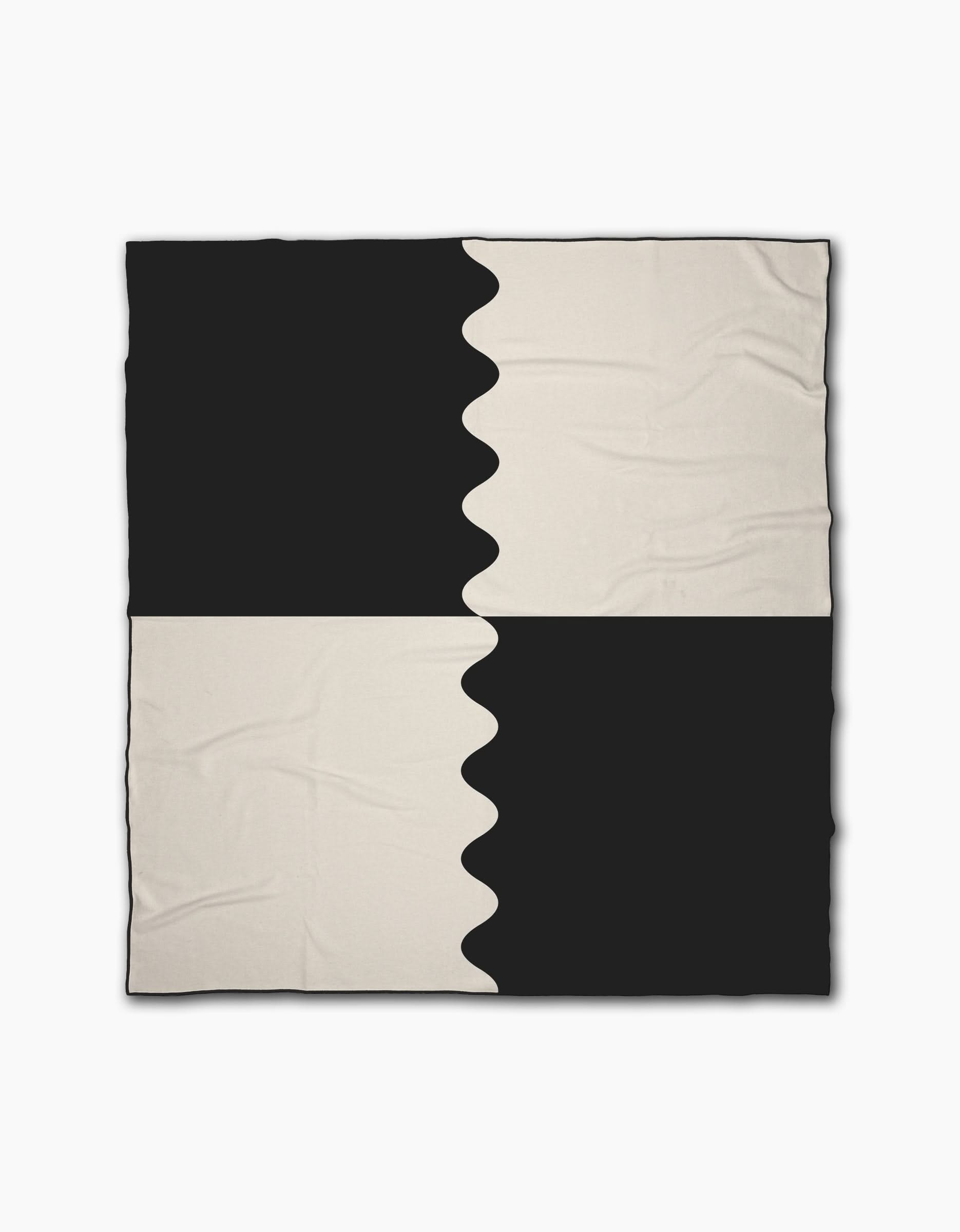 The Geometry Monochrome Waves beach blanket features a black and off-white checkered pattern with smooth and wavy color divisions for an abstract look. Made from quick-drying recycled materials, it has a slightly wrinkled texture.