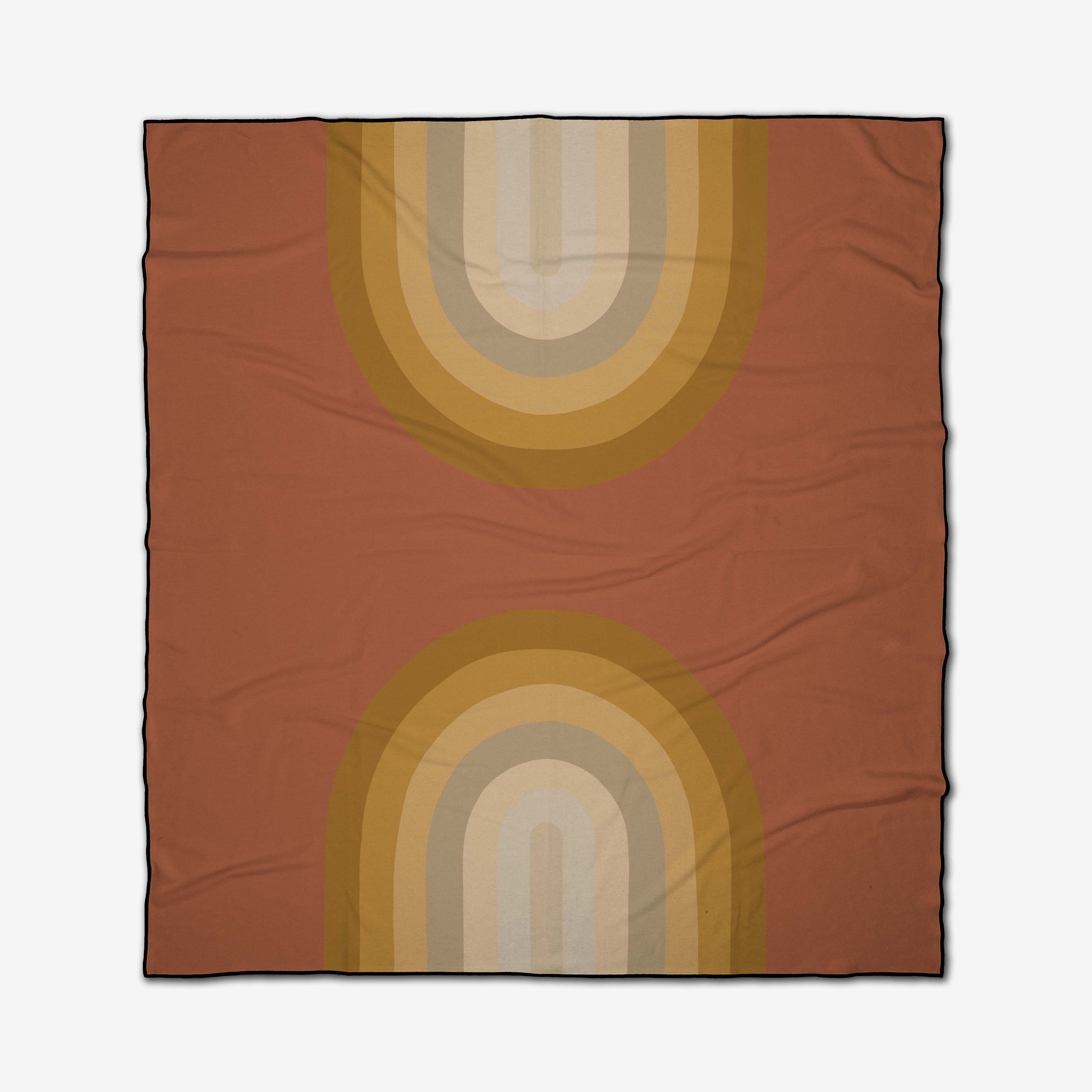 The GEOMETRY Pumpkin Spice recycled beach blanket is square, with a rust background and two mirrored retro rainbow arches in mustard, gold, beige, and tan at the top and bottom. The fabric has subtle wrinkles for a relaxed look.