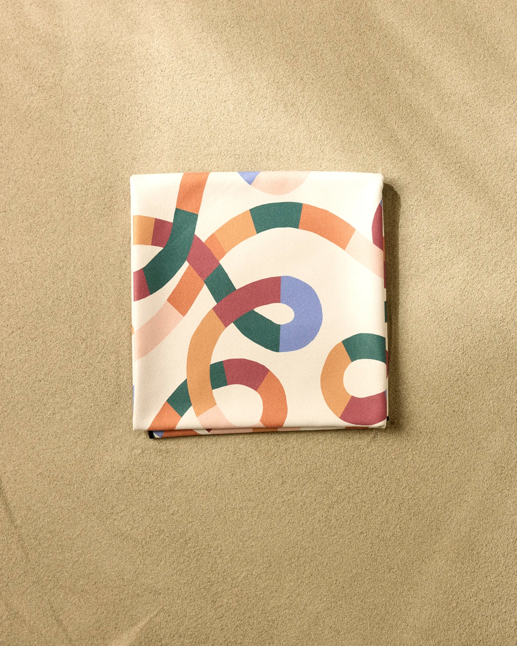A neatly folded Claire Iglesias Rainbow Squiggles Micro-loop Beach Blanket, featuring a colorful abstract swirl pattern, rests on a beige textured surface.