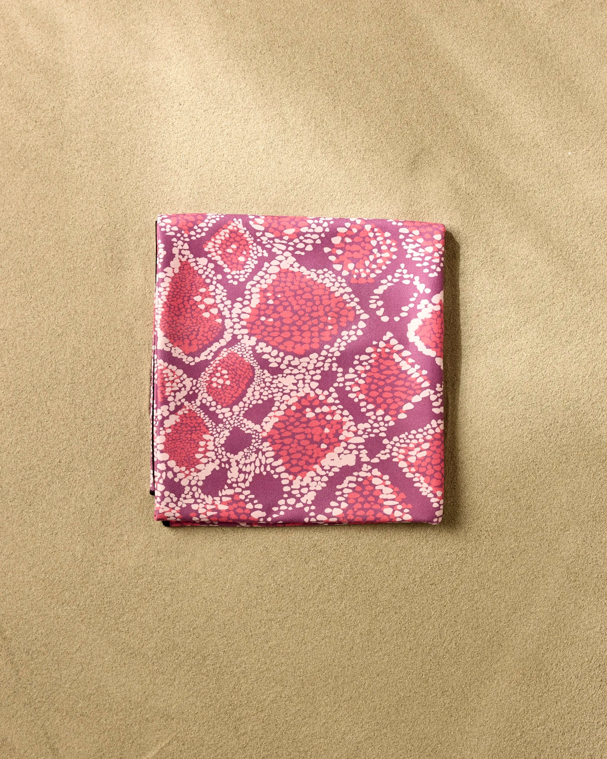 The Elisabeth Wing Vibrant Venom is a folded fabric featuring a pink and purple abstract dotted pattern, set on a textured beige background, perfect as a stylish quick-drying beach blanket.
