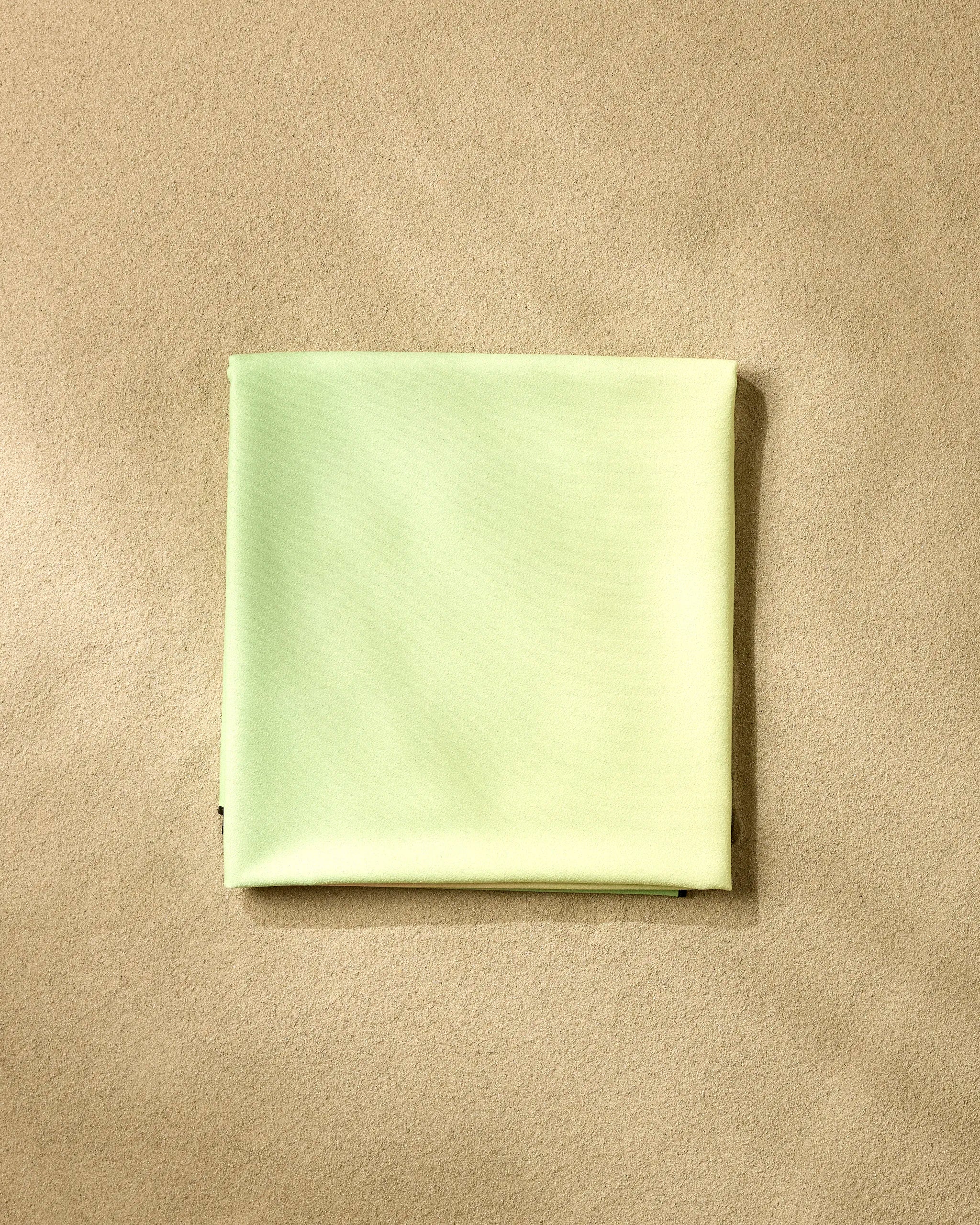 A neatly folded GEOMETRY Watermelon Gradients beach blanket made from recycled materials rests on a textured beige surface.