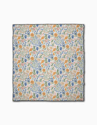 The Wildflower Vine Blush by Danelys Sidron is a square scarf with a vibrant orange, blue, and green floral print on white. Made from recycled materials, it features a thin dark border for an eco-friendly, chic finish.
