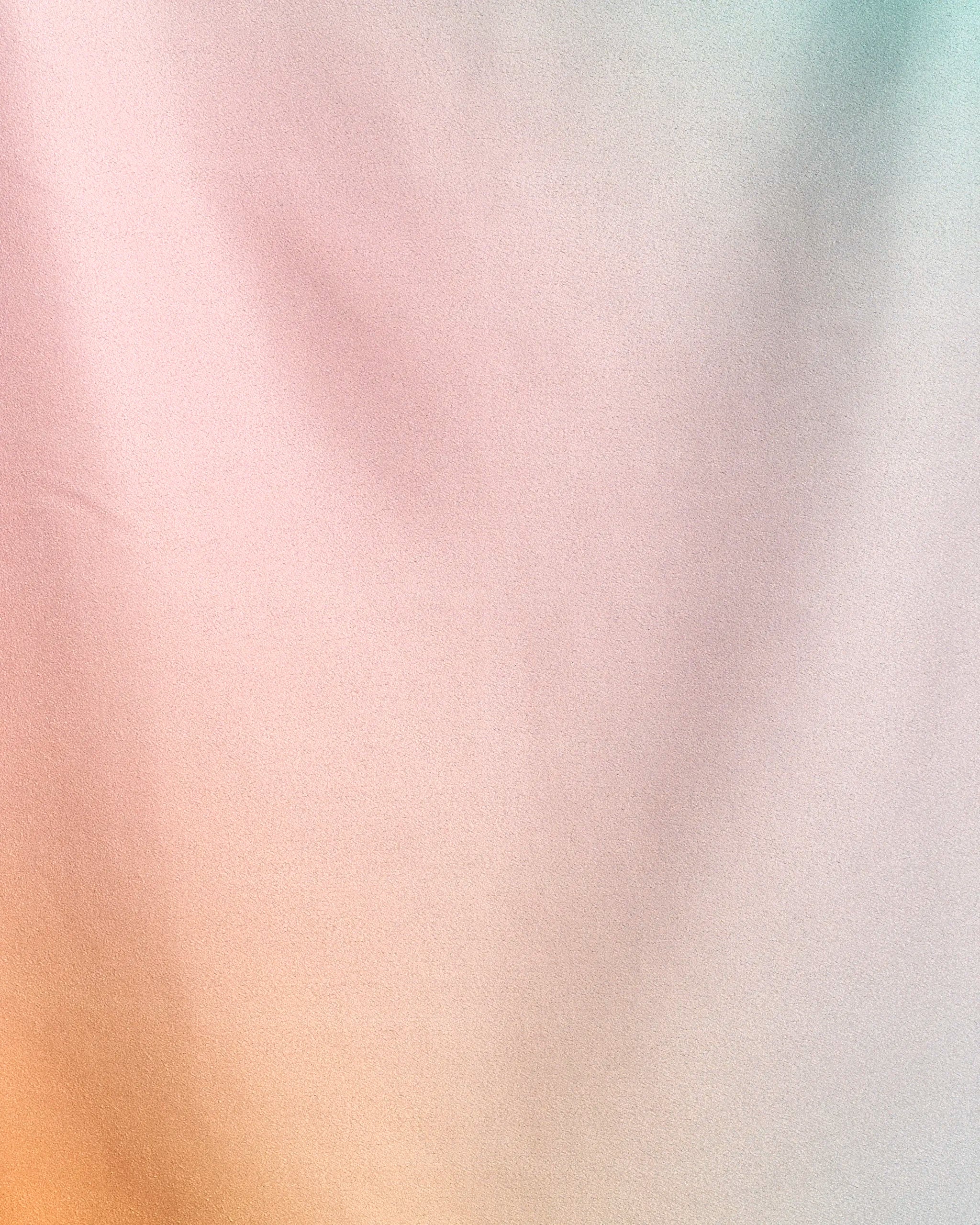 Soft pastel gradient background with pink, peach, yellow, and light blue hues reflects the dreamy, serene feel of Geometry’s Aura Flow—a quick-drying beach towel made from recycled materials for sustainable comfort.