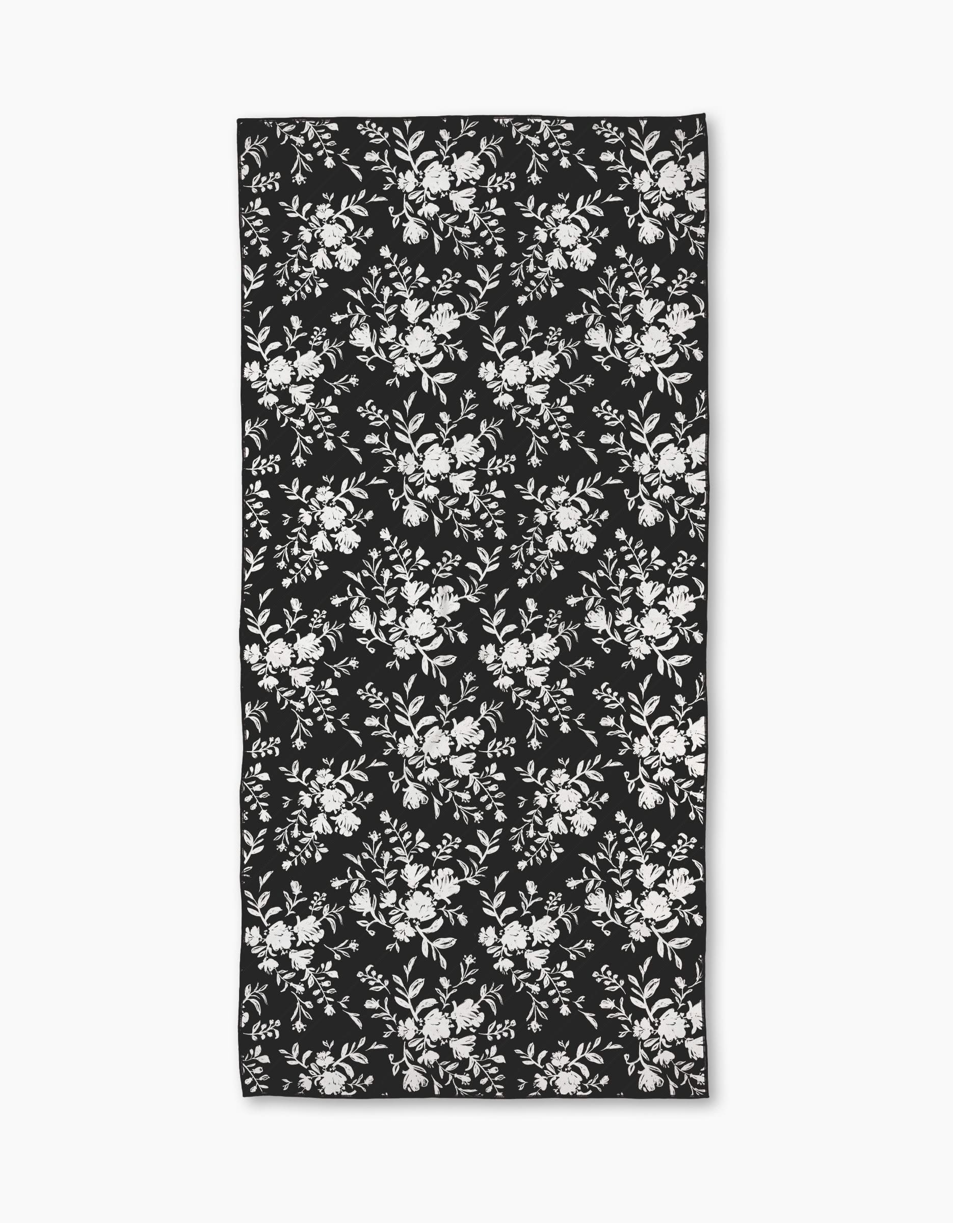 The Botanical Silhouettes Charcoal by Danelys Sidron is a rectangular micro-loop beach towel with a black base and white floral pattern, made from recycled materials for an eco-friendly touch.