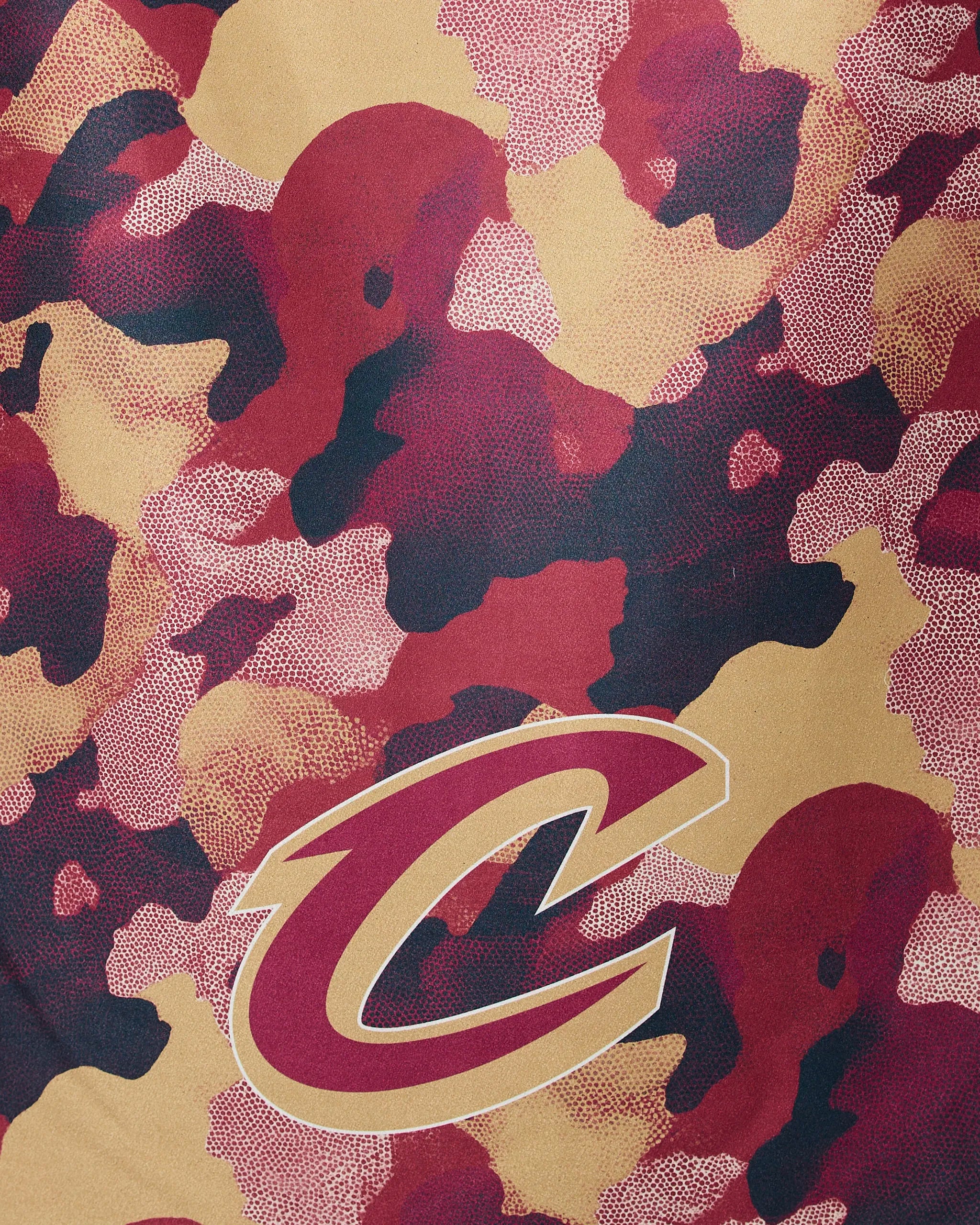 The Geometry Cavaliers Camo features a camouflage pattern in burgundy, maroon, tan, and black, accented by a large gold and burgundy Cleveland Cavaliers “C” logo outlined in white.
