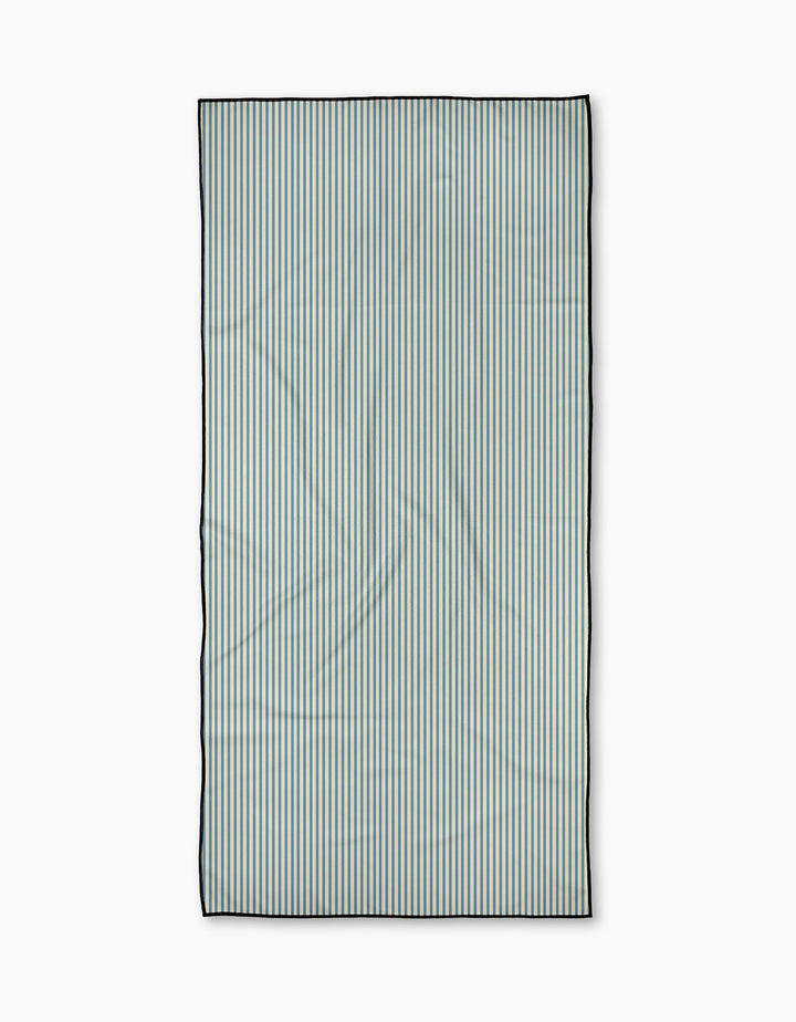 The Clean Slate beach towel by Susan Heid is rectangular and quick-drying, featuring thin, evenly spaced vertical blue and white stripes with a dark border, shown on a plain white background.