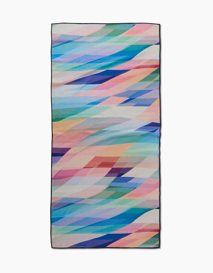 The Eventide Micro-loop Beach Towel by Rachel Parker features multicolored geometric diagonal shapes on white. Made with recycled materials, it offers a quick-drying, eco-friendly beach experience.