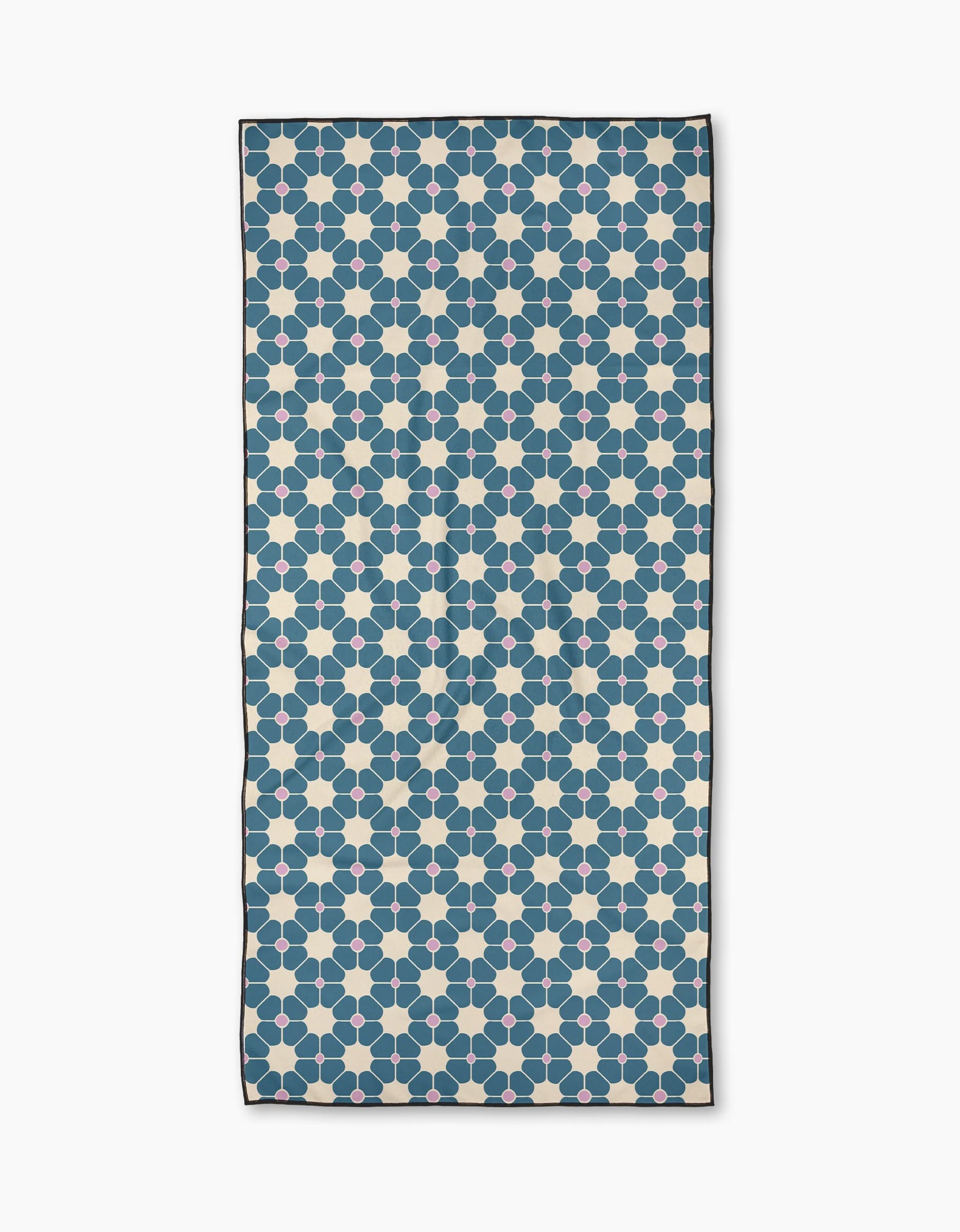 Flora Tile Blue is a rectangular micro-loop beach towel made from recycled materials, with a blue hexagon and beige circle geometric pattern on white, finished with a thin black border.