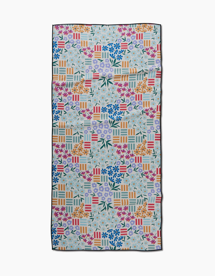 The Floral Garden beach towel by Charlie Rowan Designs is made from recycled materials and features a colorful geometric and floral pattern in blue, pink, orange, and green. Quick-drying—perfect for your next trip to the shore.