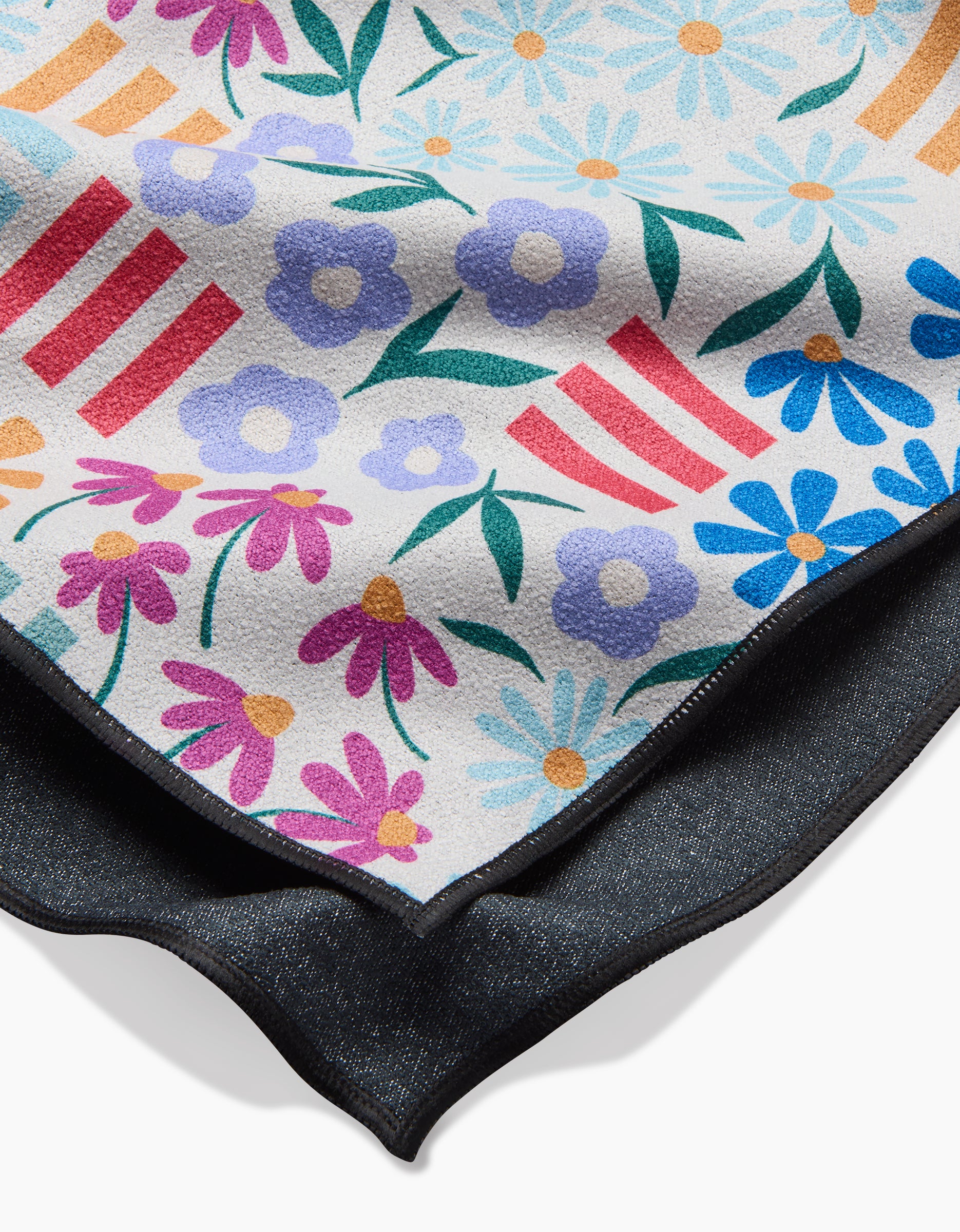 A close-up of the Charlie Rowan Designs Floral Garden beach towel, showcasing a vibrant floral pattern with red and white stripes, crafted from recycled materials and set against a dark fabric background.
