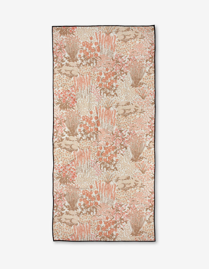 The Hufton Studio Garden Bloom towel is a rectangular beach towel with clusters of peach, pink, beige, and brown florals on quick-drying recycled fabric, finished with a dark thin border.