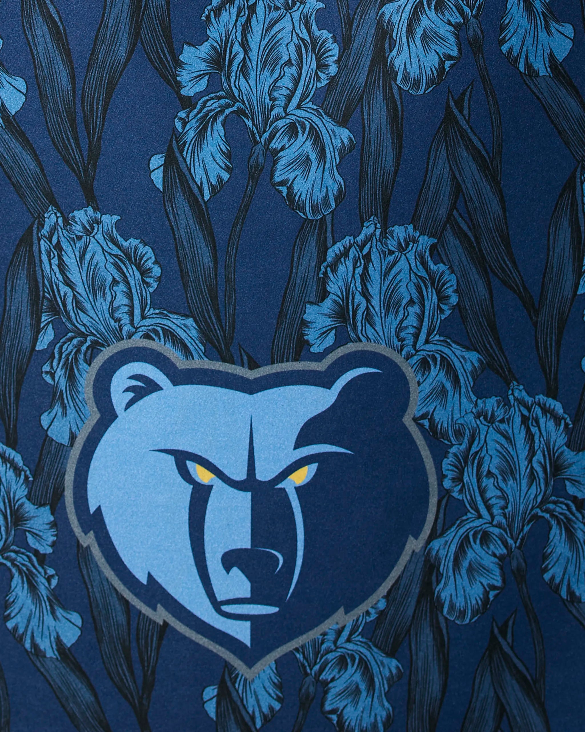 The Grizzlies Floral by Geometry features a stylized bear head logo with yellow eyes, centered on a blue background adorned with illustrated iris flowers and dark leaves.